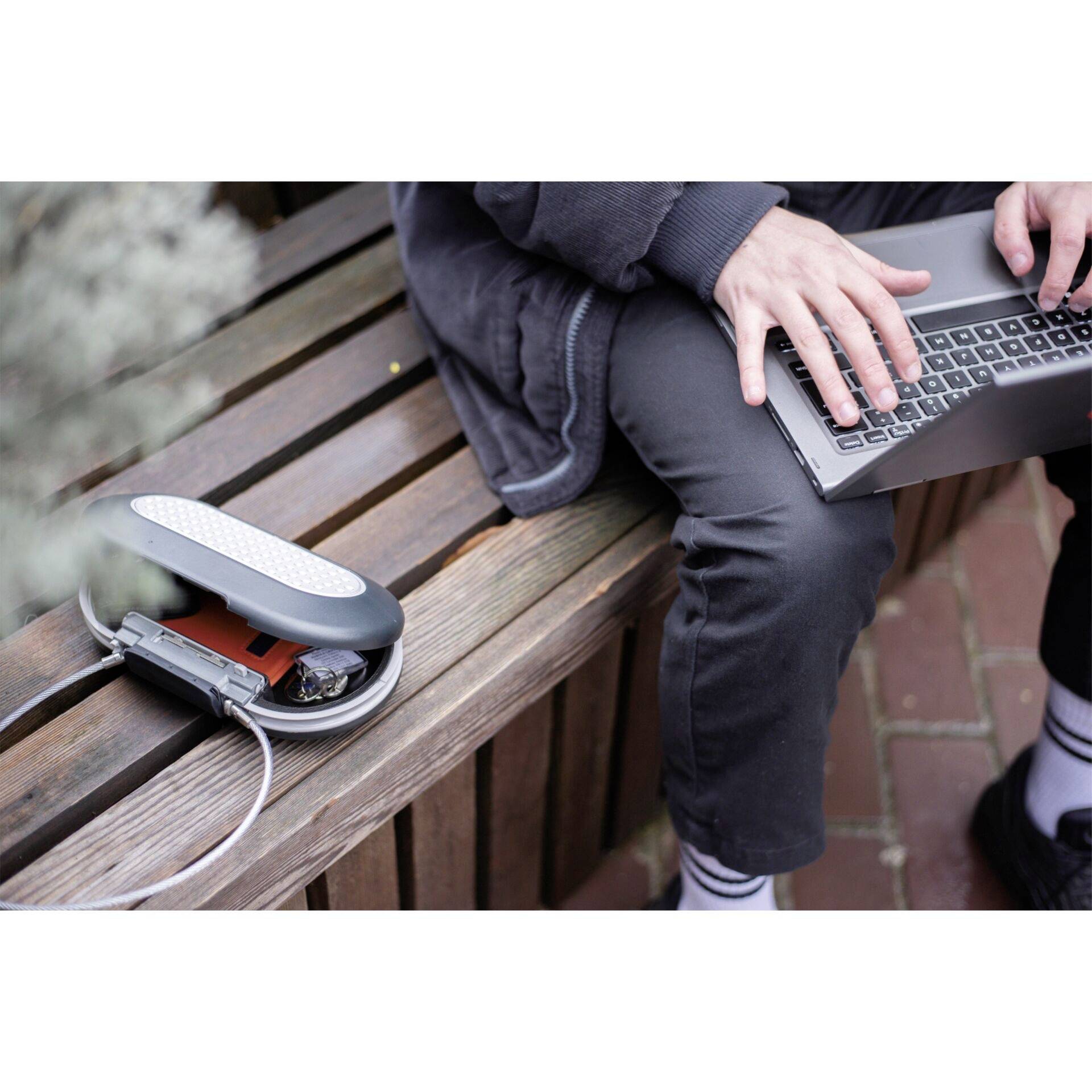 Une personne est assise sur un banc en bois et travaille sur un ordinateur portable. À côté se trouve un boîtier de disque dur ouvert avec un disque dur visible.