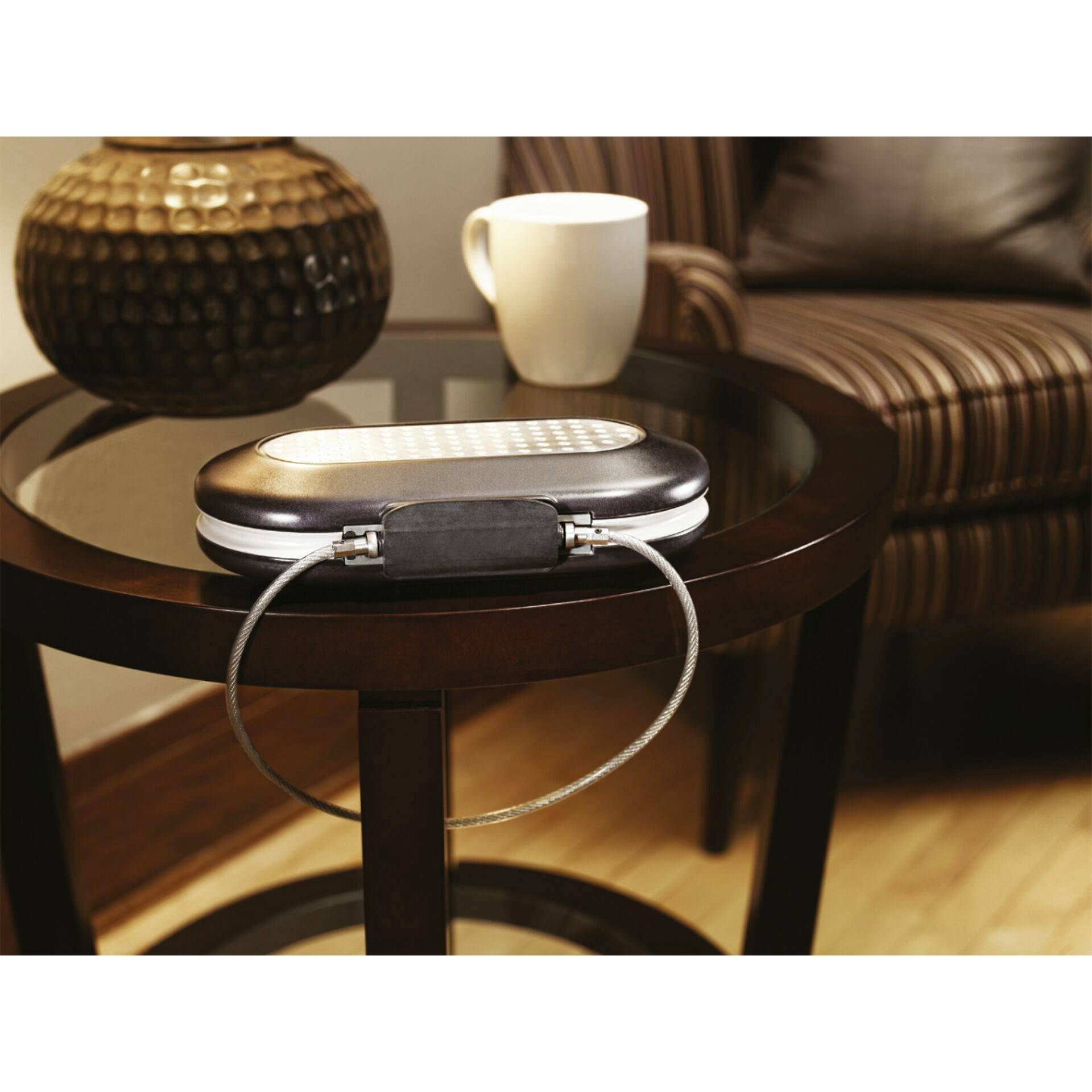 Un petit dispositif de rangement fermé sur une table ronde en bois, à côté d'une tasse, devant un fauteuil rembourré rayé.