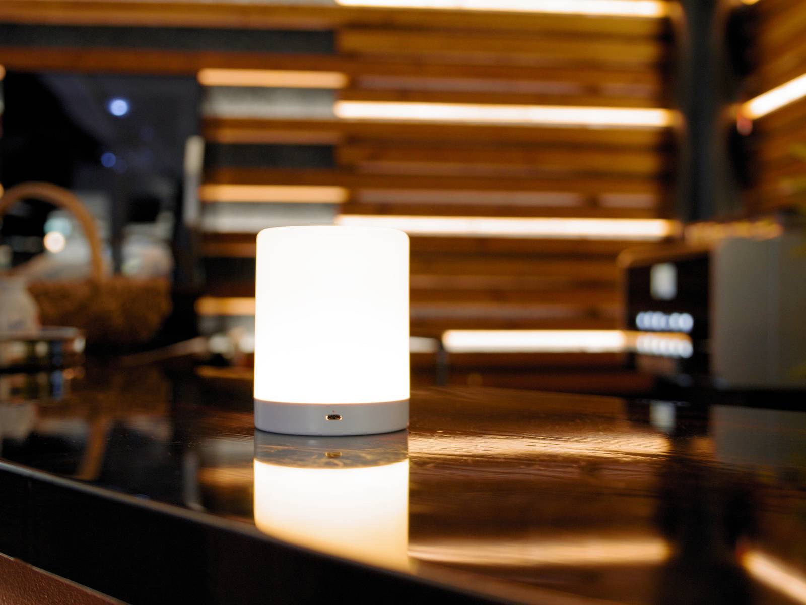 Une lampe de table à la lumière douce et chaleureuse est posée sur une table brillante et sombre, devant un fond de panneaux en bois.