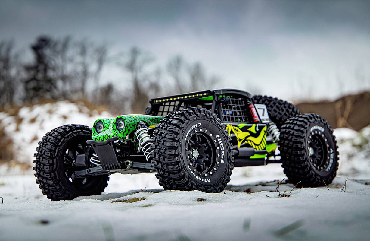 Une voiture télécommandée aux grandes roues robustes et à la peinture voyante vert et noir est positionnée en biais dans la neige.