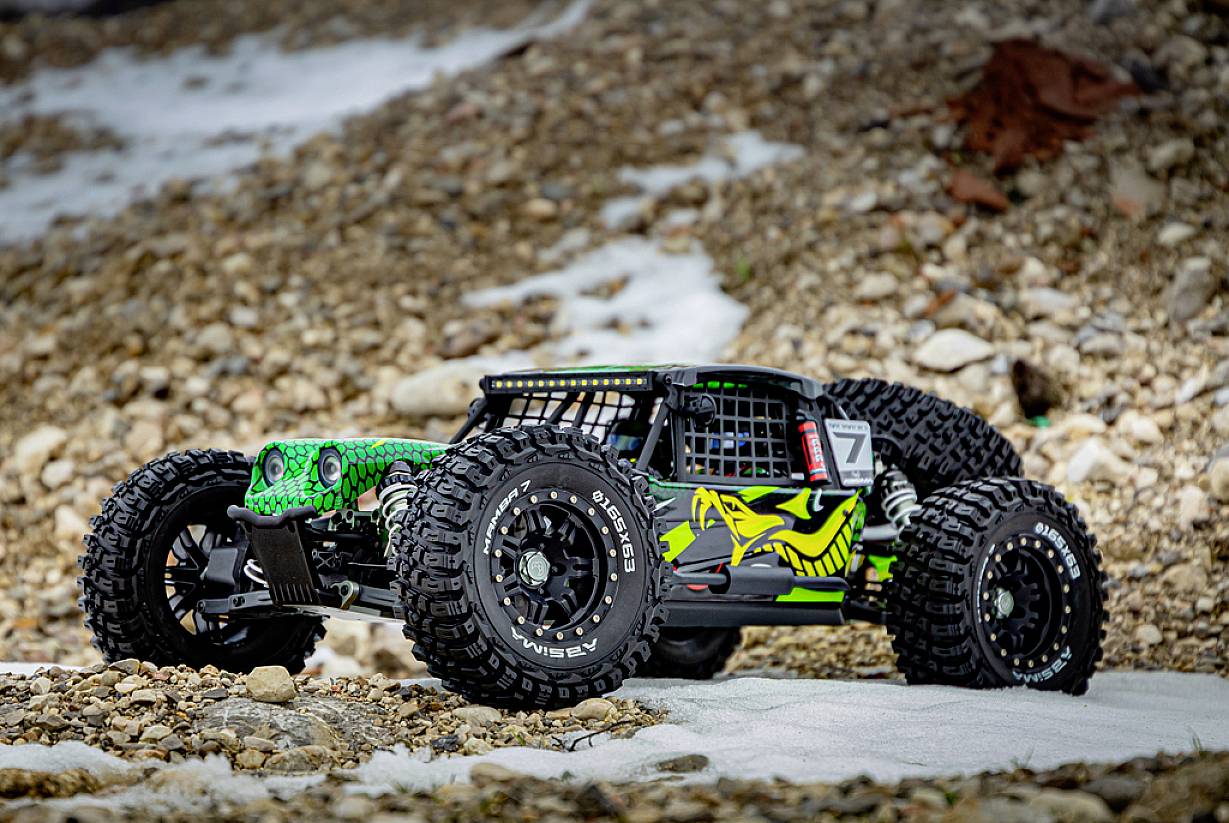 Une voiture télécommandée au design tout-terrain roule sur une surface rocheuse. La voiture possède de grandes roues et un design vert distinctif.