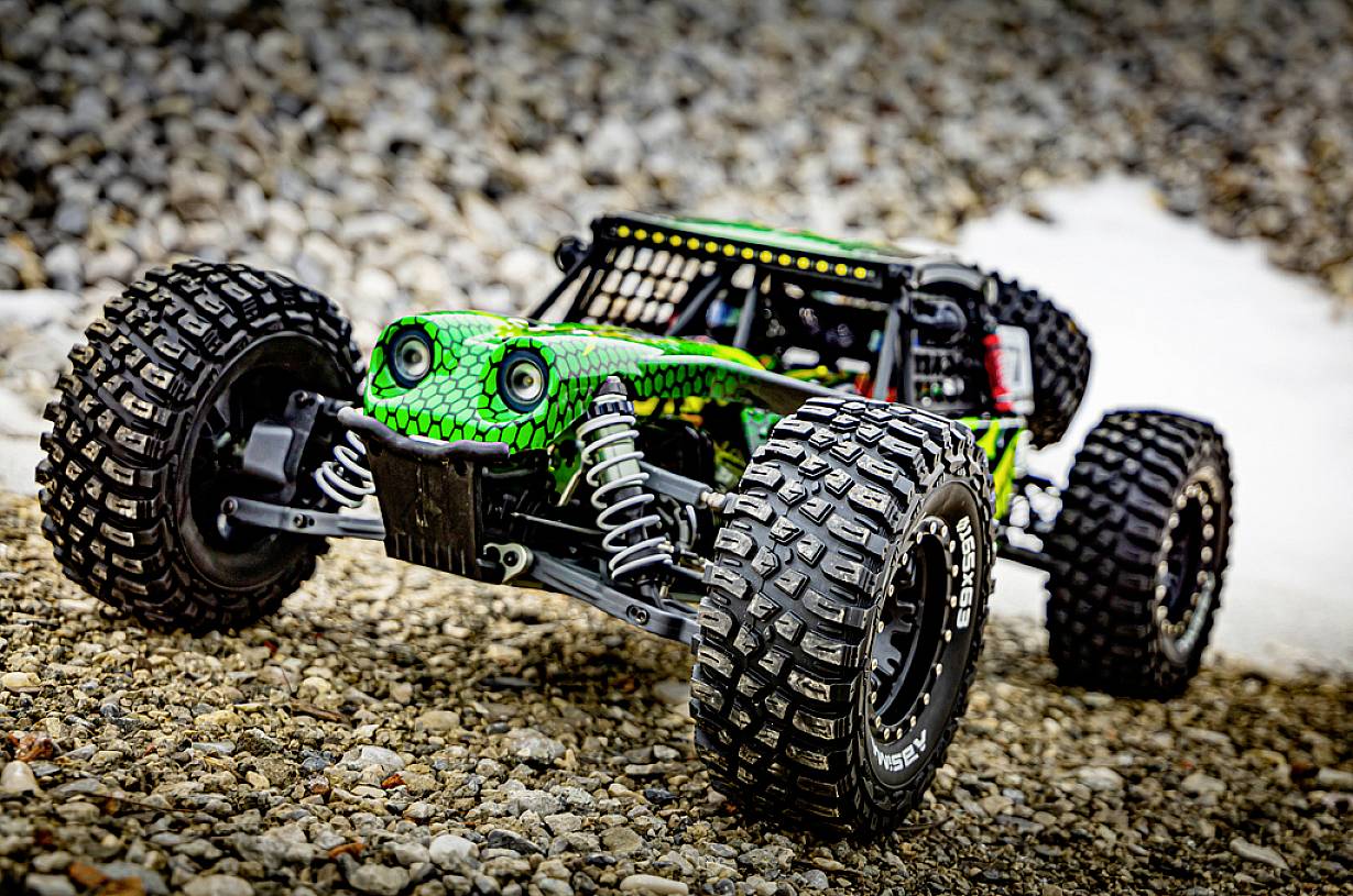 Voiture télécommandée avec un motif de serpent vert, roulant sur une route de gravier. Les grandes roues et la suspension sont visibles.