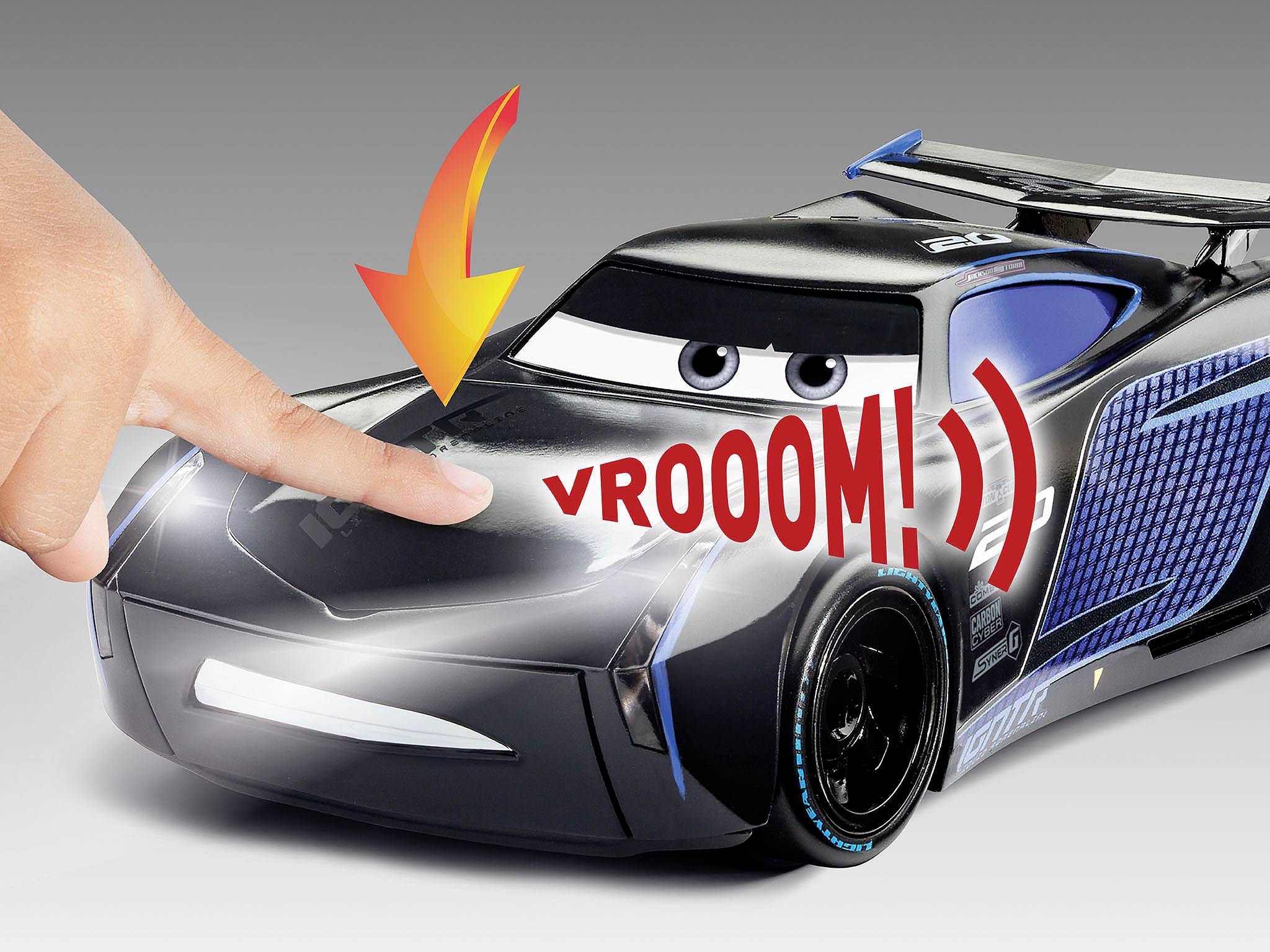 Un doigt appuie sur la voiture jouet aux grands yeux et portant le texte « VROOOM ! ». Une flèche pointe vers le point de contact.