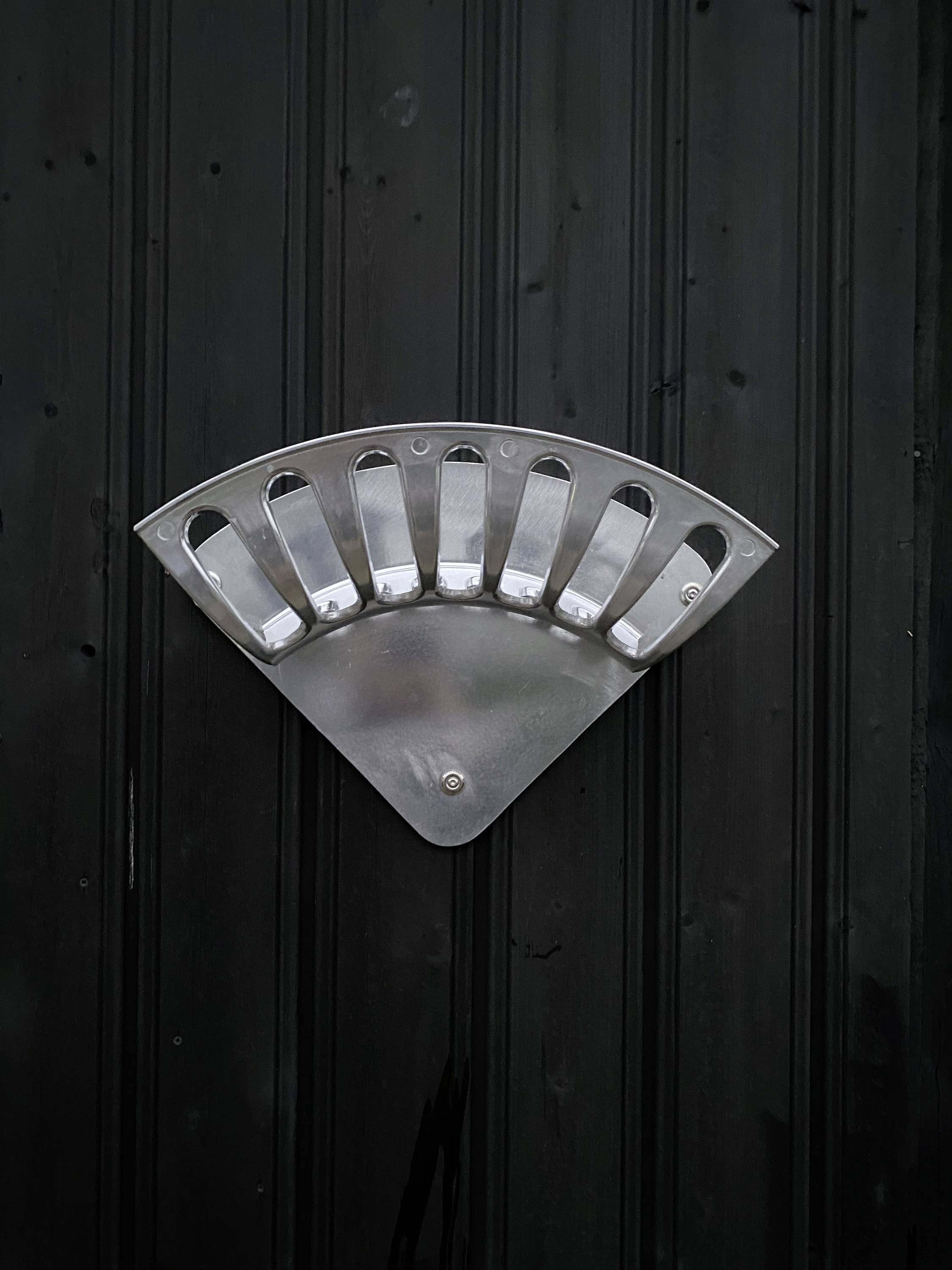 Œuvre d'art métallique en forme d'éventail sur fond noir, montée sur une surface verticale.