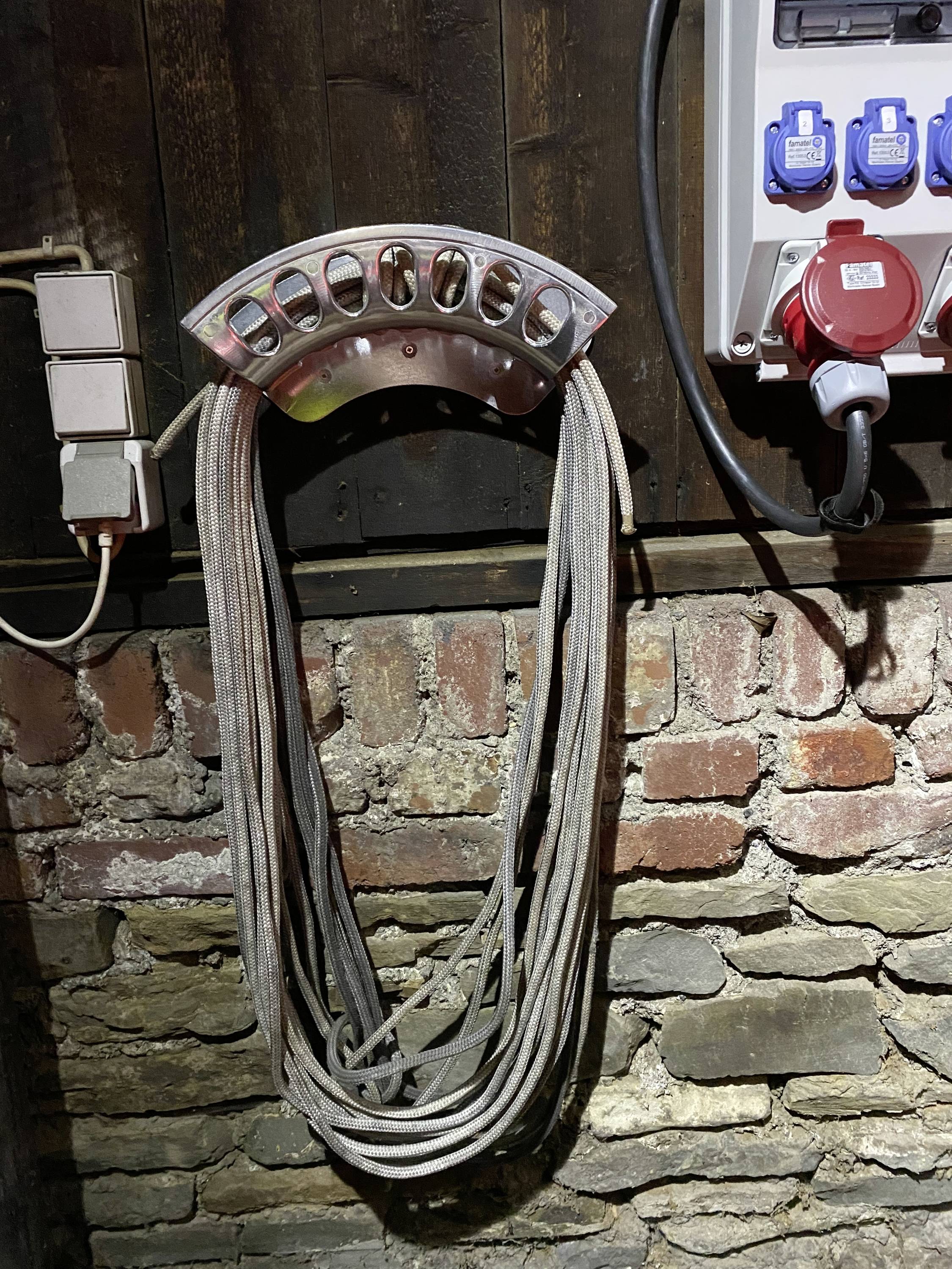 Un faisceau de câbles pend à un support fixé à un mur de briques. À côté, on peut voir des prises électriques et un branchement électrique.