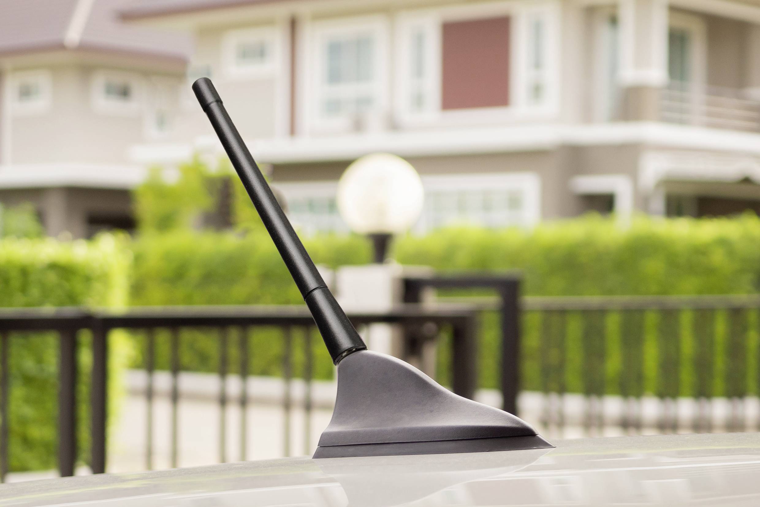 Antenne automatique sur le toit d'un véhicule, avec une maison résidentielle floue et un jardin vert en arrière-plan.