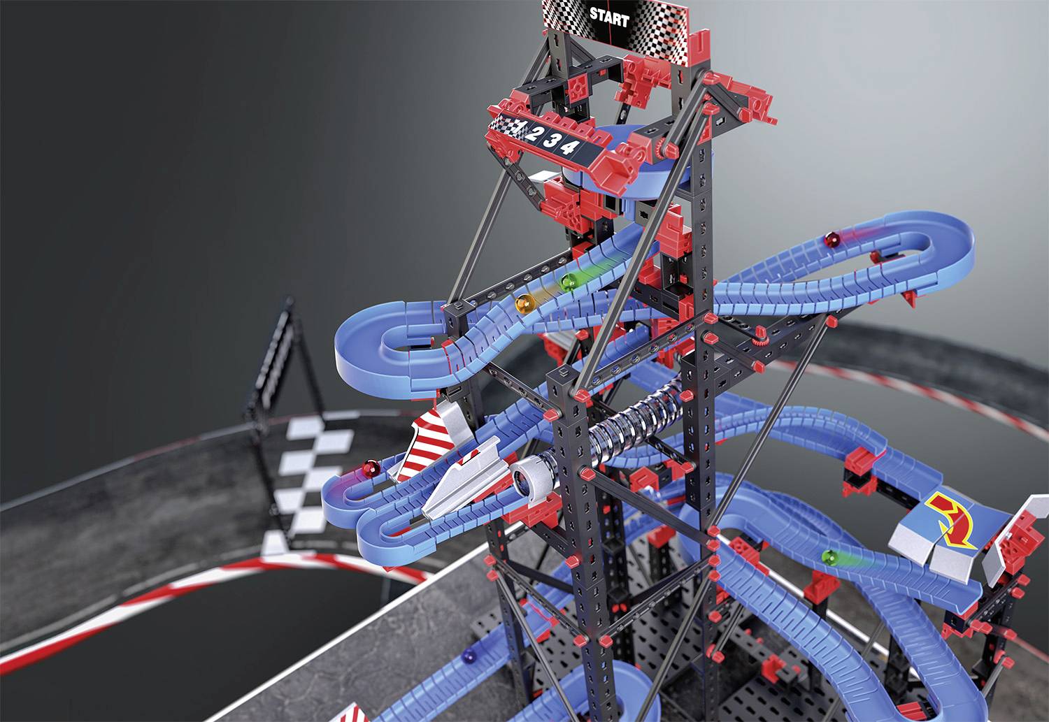 Une tour de circuit de billes composée de pièces modulaires bleu et rouge, sur laquelle des billes parcourent des trajectoires sinueuses, avec une ligne de départ en haut.