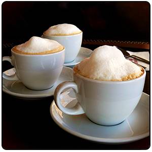 Trois tasses de cappuccino avec de la mousse de lait reposent sur des soucoupes sur une table.