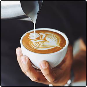 Une personne verse artistiquement du lait mousseux dans une tasse de café pour créer un motif en forme de cœur.