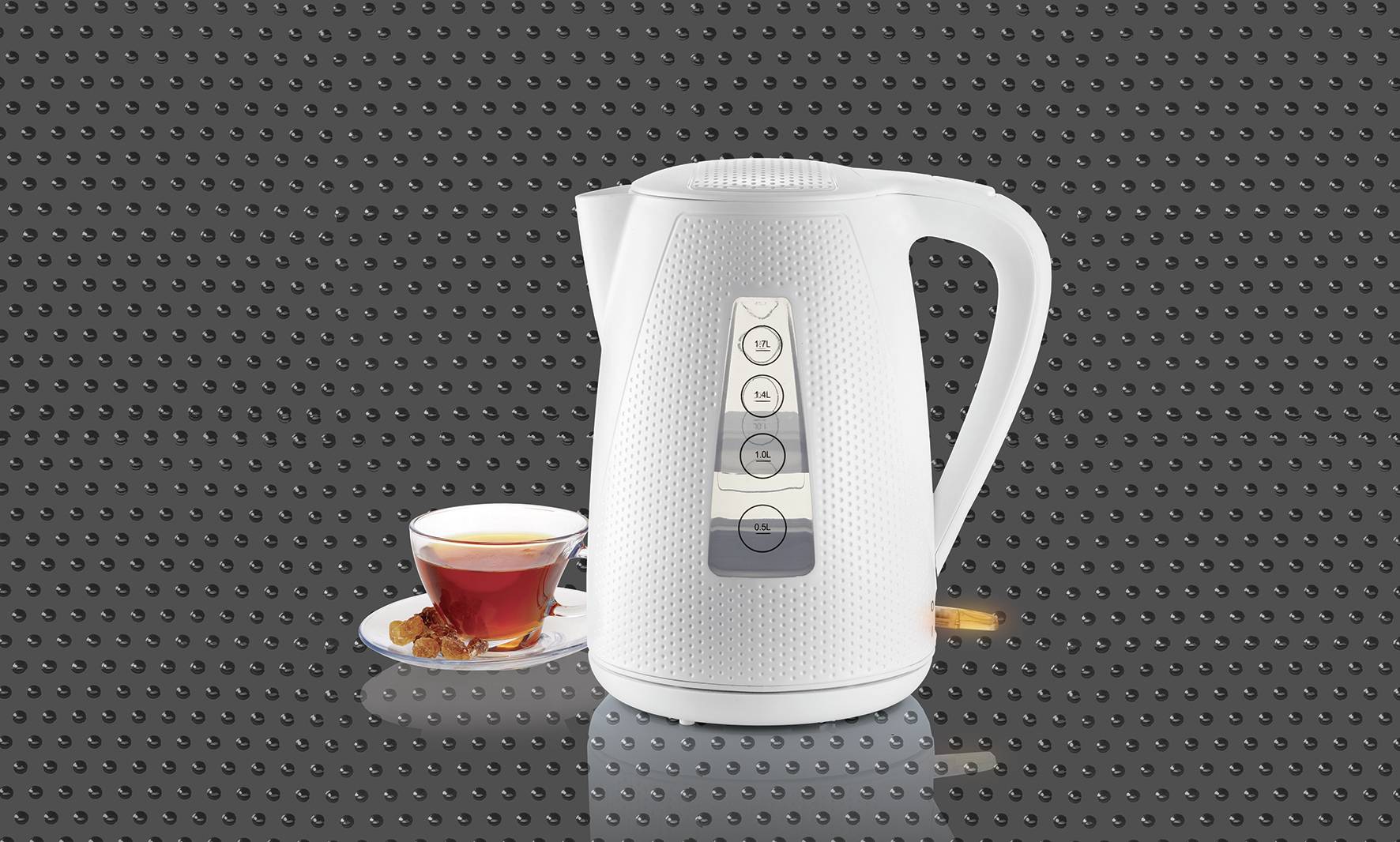 Un bouilloire blanche est placée devant un fond sombre, avec un verre de thé sur une soucoupe à côté.