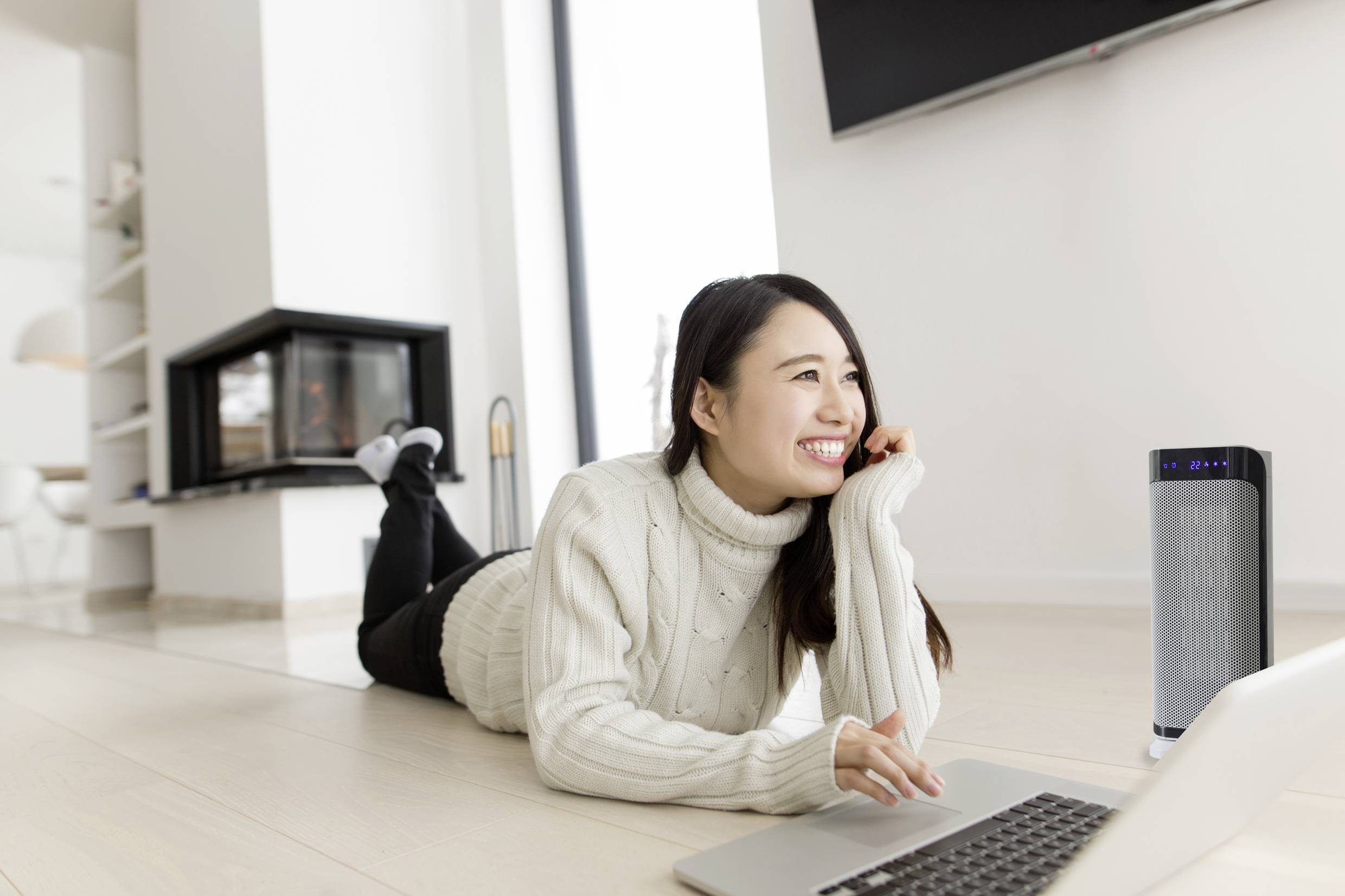 Une personne souriante est allongée par terre, travaille sur un ordinateur portable avec un purificateur d'air à proximité dans la pièce.
