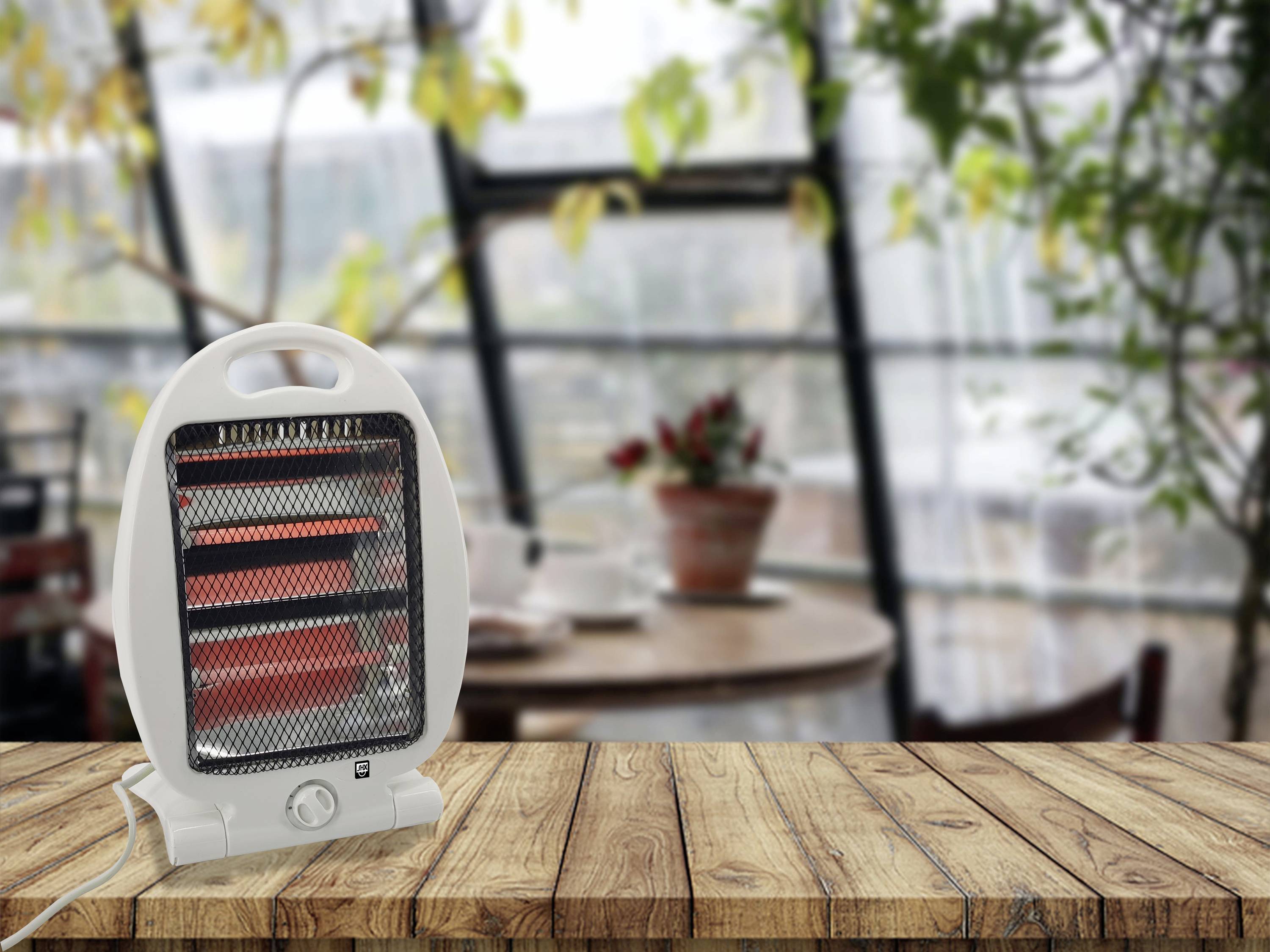 Un petit chauffage électrique d'appoint est posé sur une table en bois dans une pièce chaleureuse avec de grandes fenêtres et des plantes en pot.