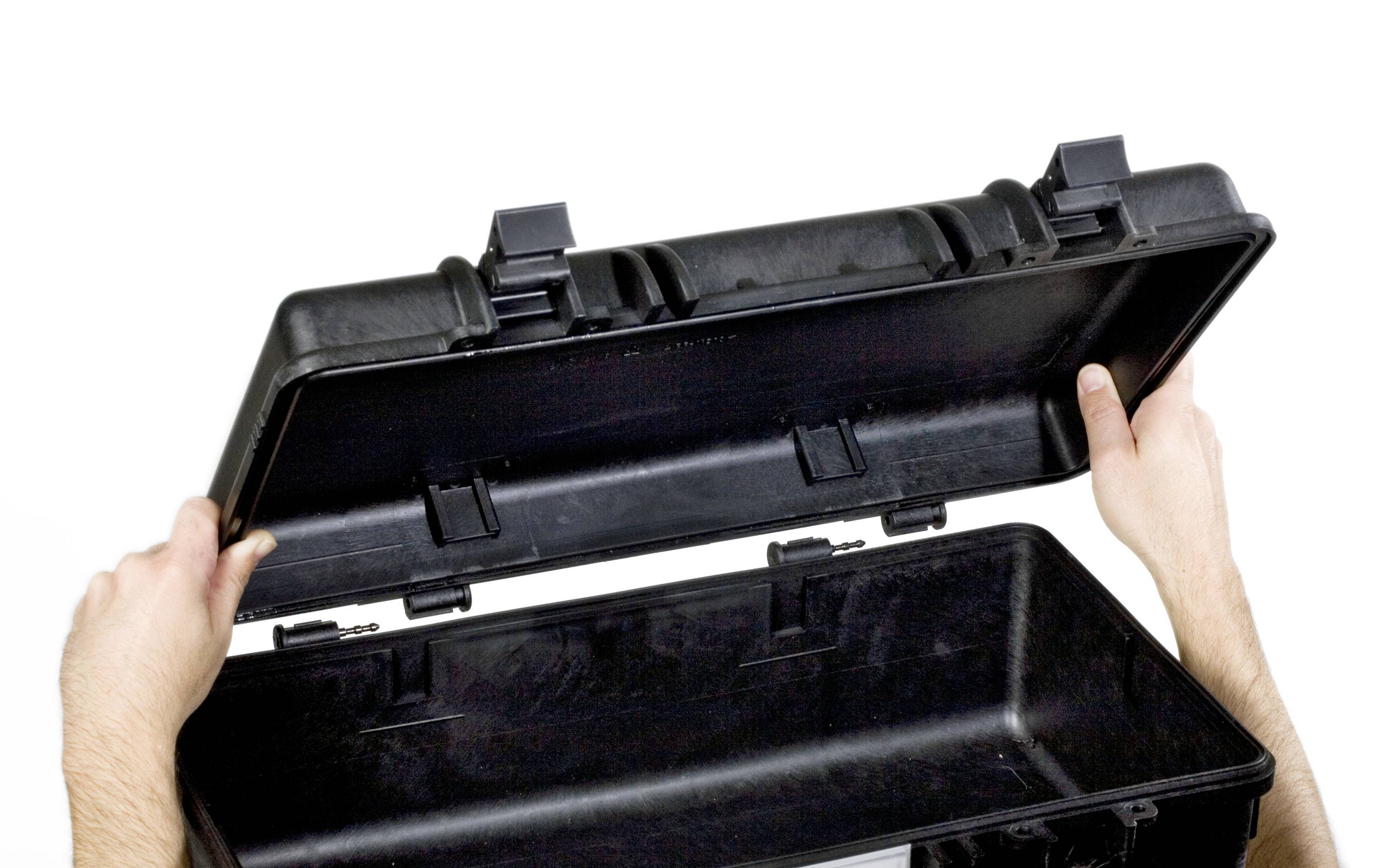 Deux mains ouvrent une valise noire et robuste. La valise est vide et fabriquée dans un matériau résistant.