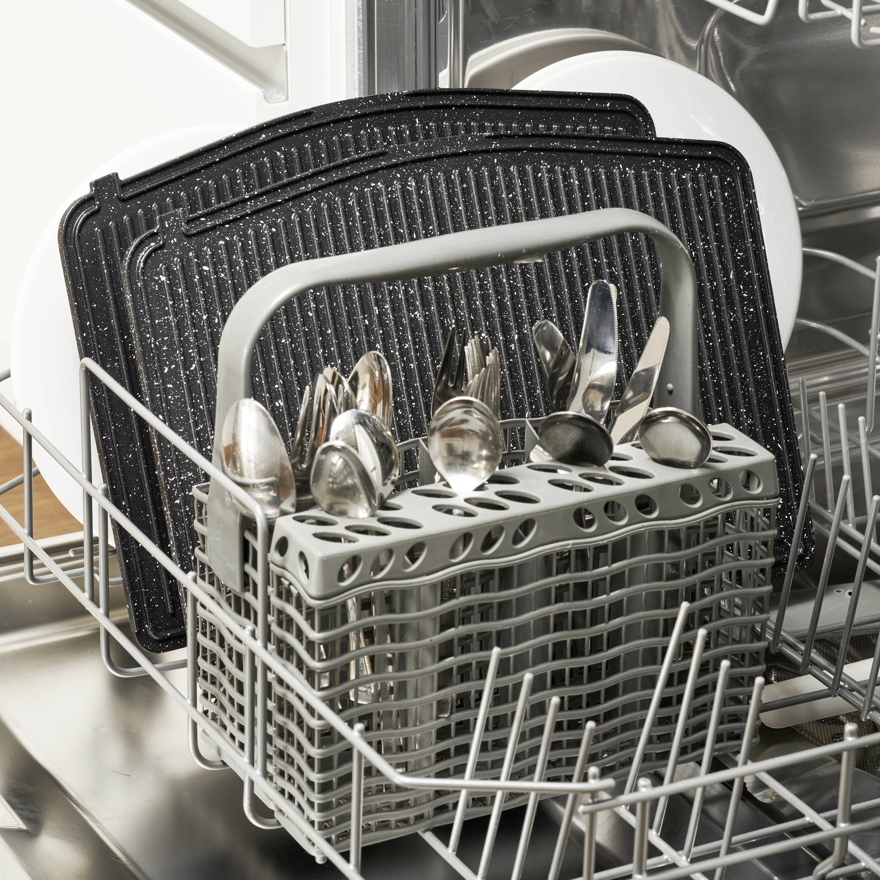 Un lave-vaisselle à la porte ouverte montre des couverts dans un support et plusieurs plateaux noirs en arrière-plan.