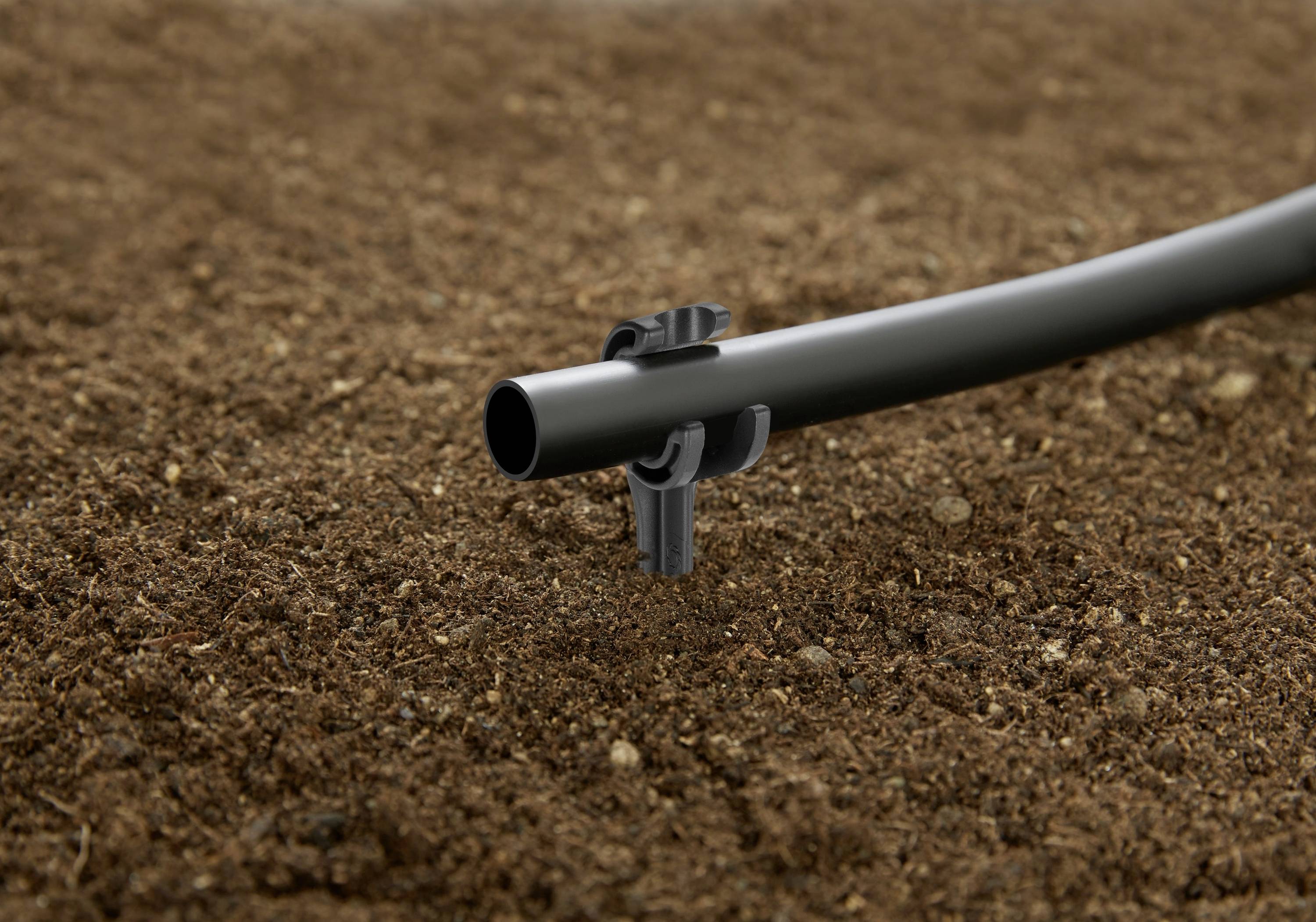 Un tuyau d'irrigation goutte à goutte positionné sur le sol, maintenu par un clip, illustrant un système efficace de distribution d'eau pour le jardinage ou l'agriculture.