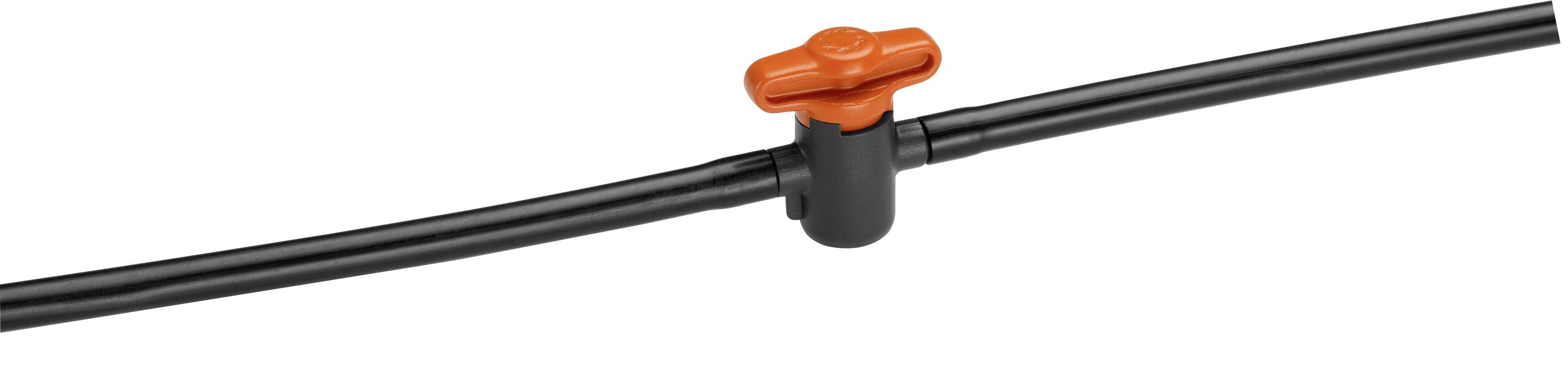 Tuyau d'irrigation noir avec une vanne d'arrêt rouge au milieu. Vanne permettant de contrôler le flux d'eau dans un système d'irrigation de jardin.