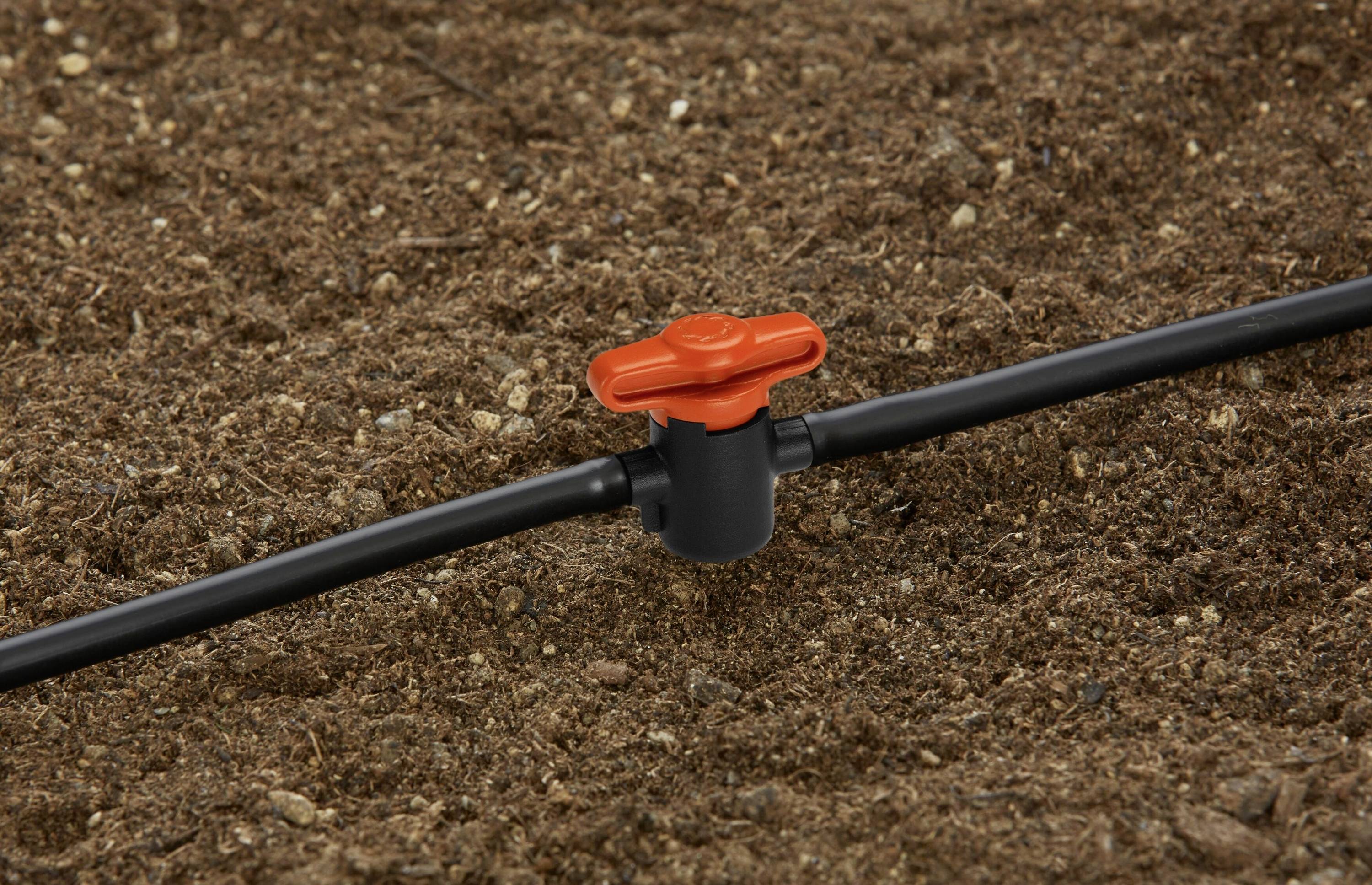 Un tuyau d'irrigation noir avec une vanne rouge sur un sol terreux brun, faisant partie d'un système d'irrigation goutte à goutte.