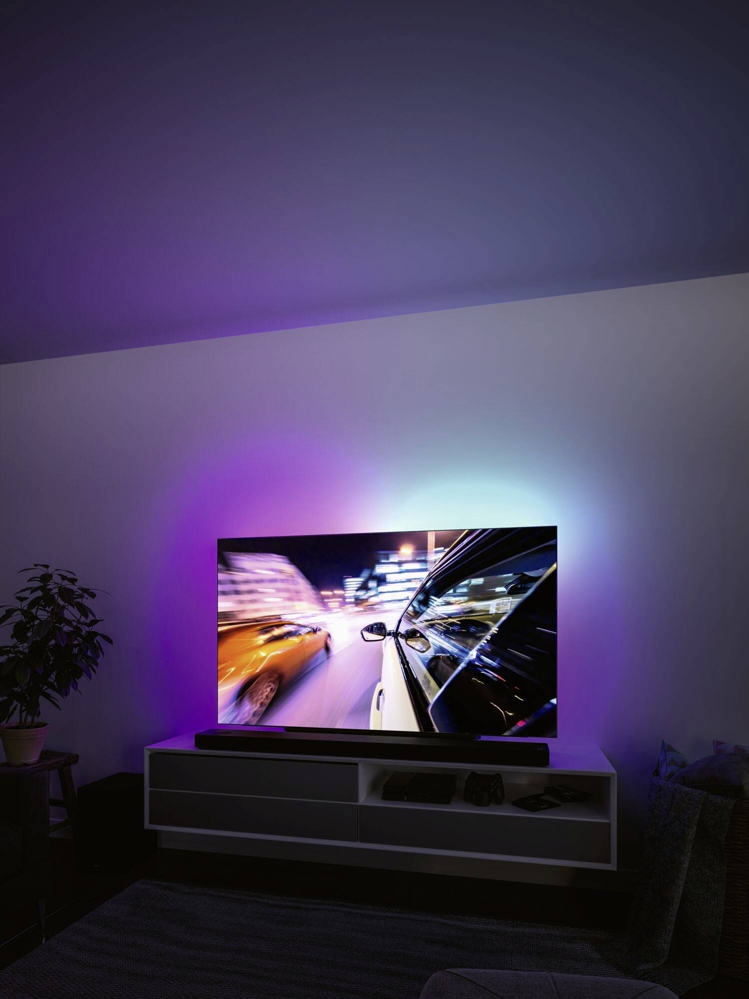 Un téléviseur moderne affiche une course nocturne aux couleurs vives, reflétant la lumière dans la pièce, et est posé sur une étagère blanche.