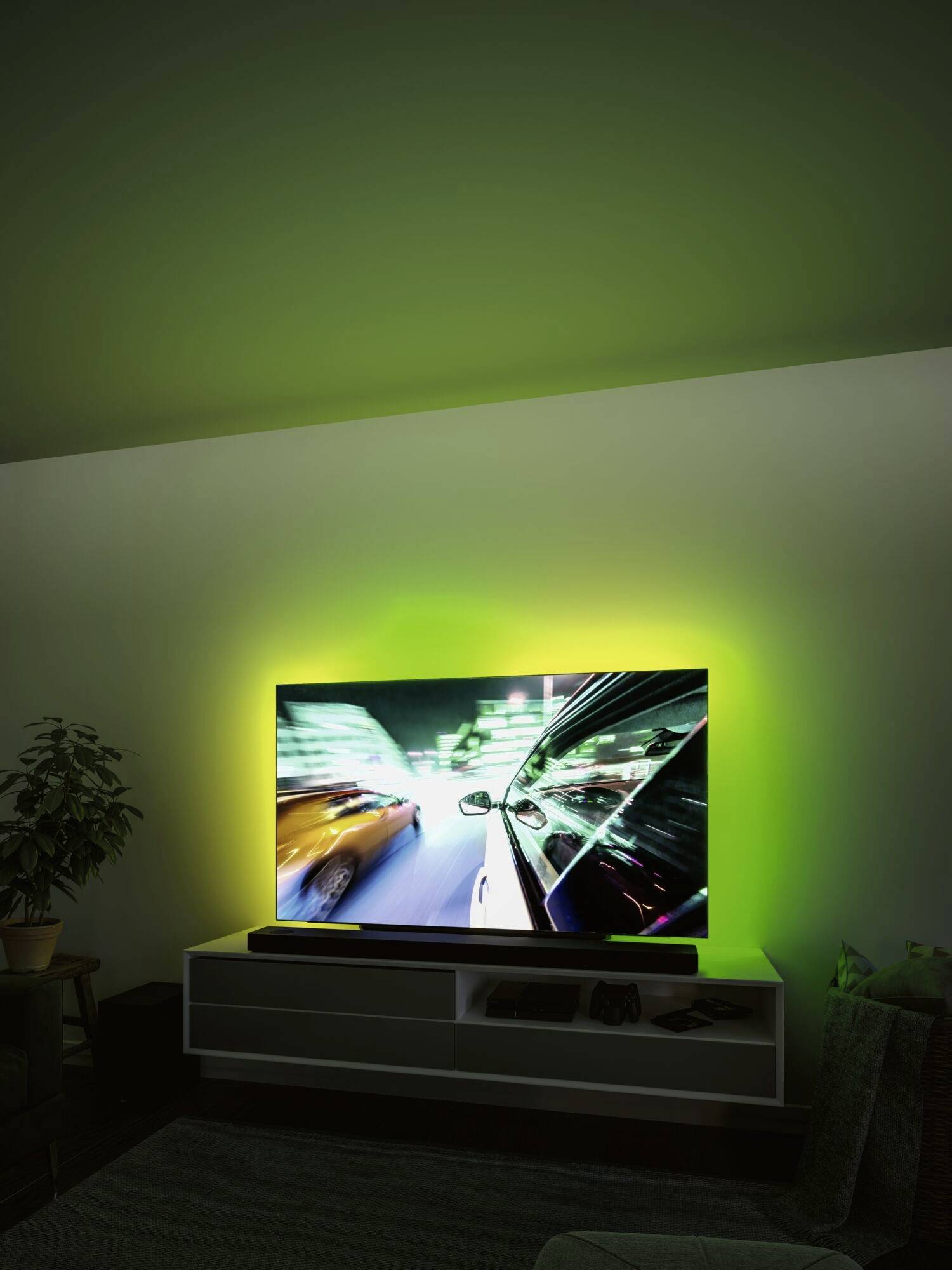 Un téléviseur affiche une scène de course effrénée avec des voitures floues, baignées dans une lumière verte ambiante dans une pièce sombre.