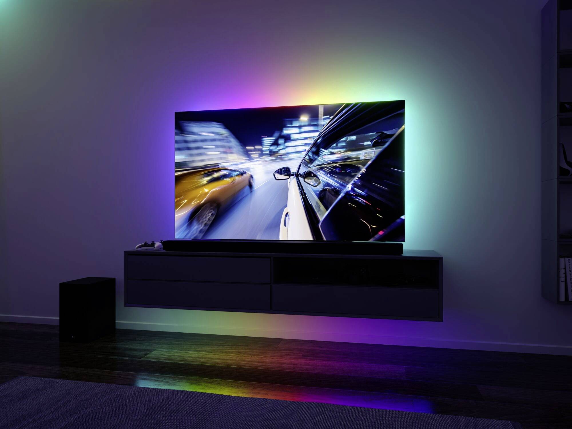 Un téléviseur à écran plat affiche un trajet automobile dynamique de nuit, entouré d'effets lumineux colorés projetés sur le mur.