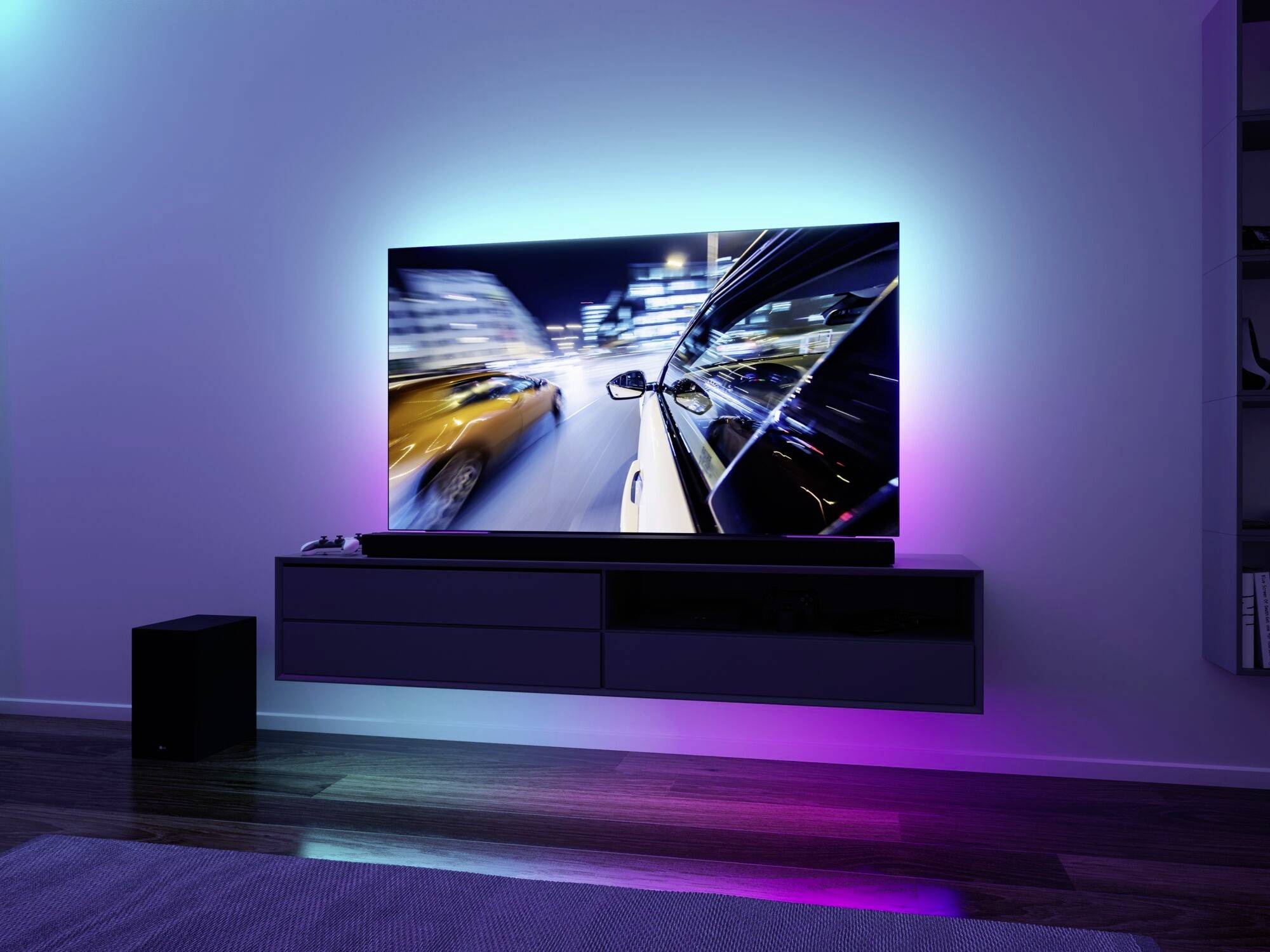 Aménagement intérieur moderne d'un salon avec une télévision montrant un paysage urbain flou la nuit. Éclairage coloré en arrière-plan du mur.