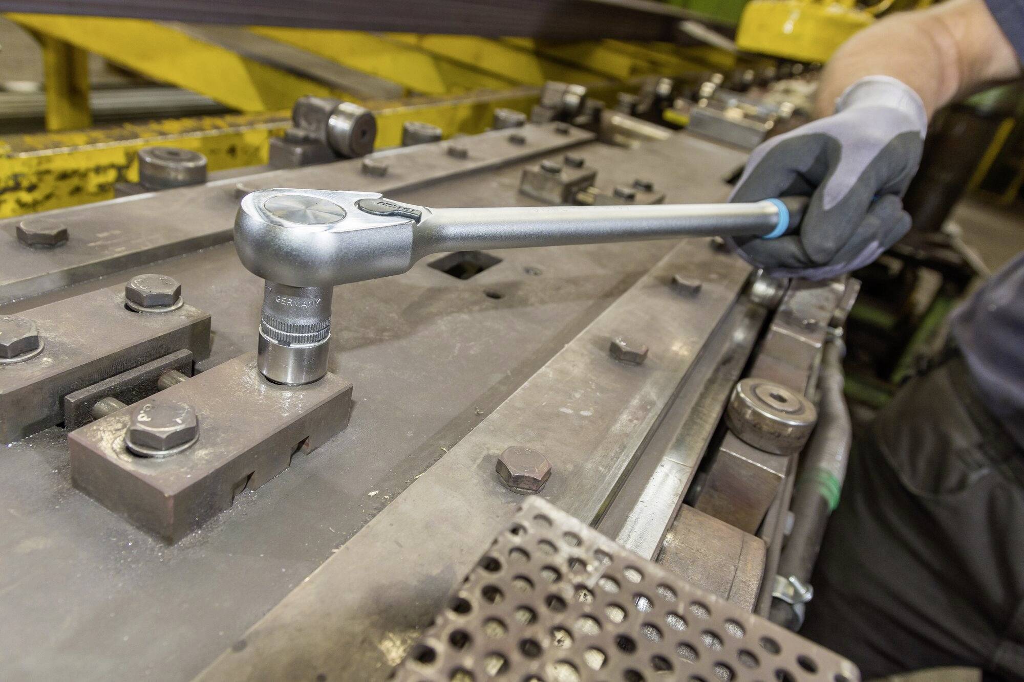 Une personne utilise une clé à molette pour serrer une grande machine métallique dans un environnement industriel.