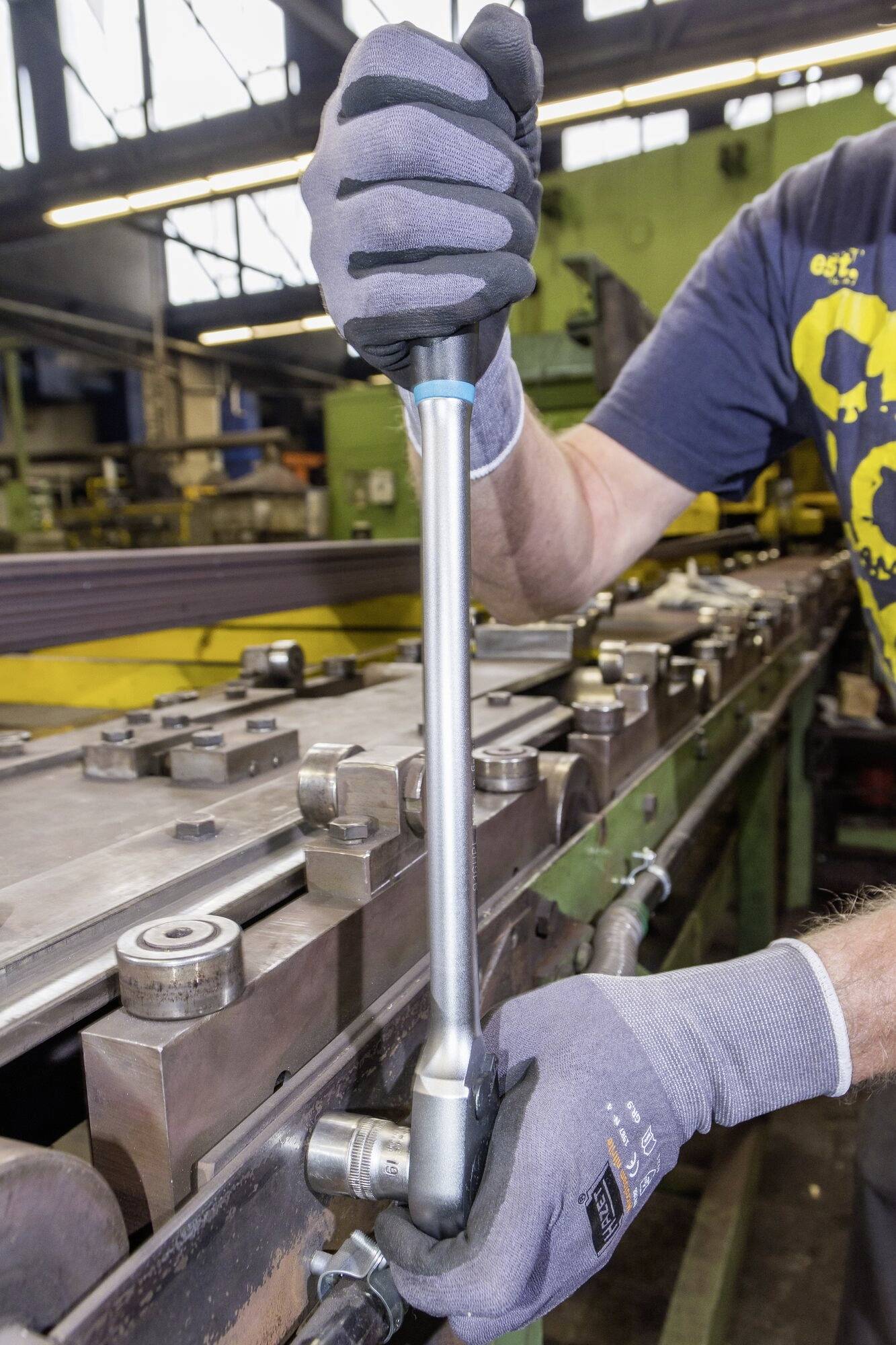 Une personne portant des gants de travail serre une vis avec une clé dynamométrique sur une machine industrielle dans un atelier.