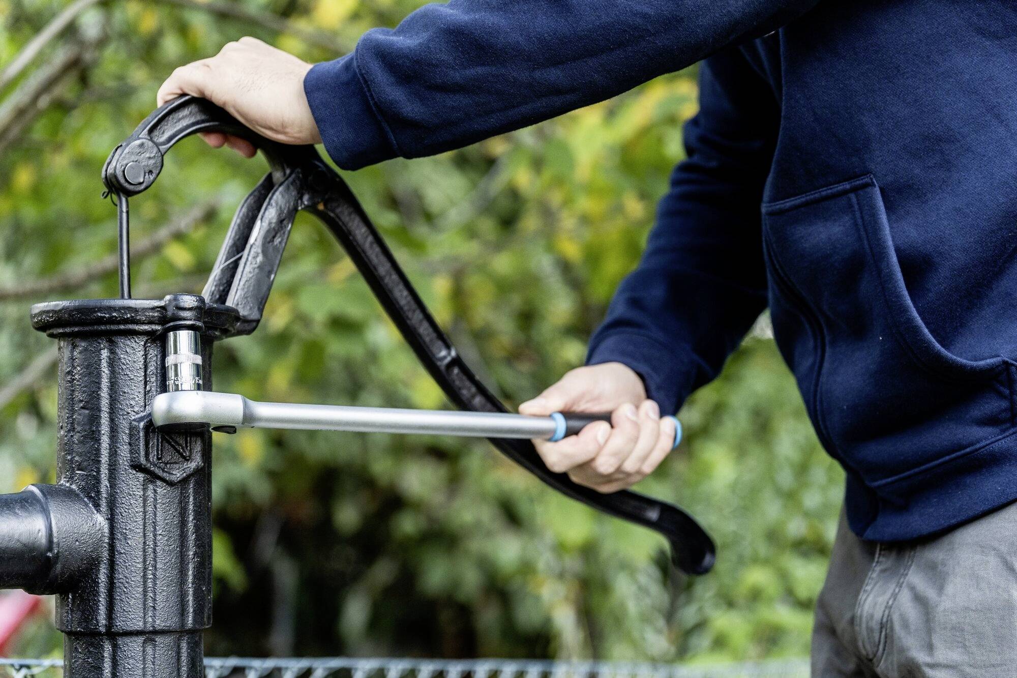 Une personne portant un pull bleu actionne une pompe à eau manuelle à l'extérieur.