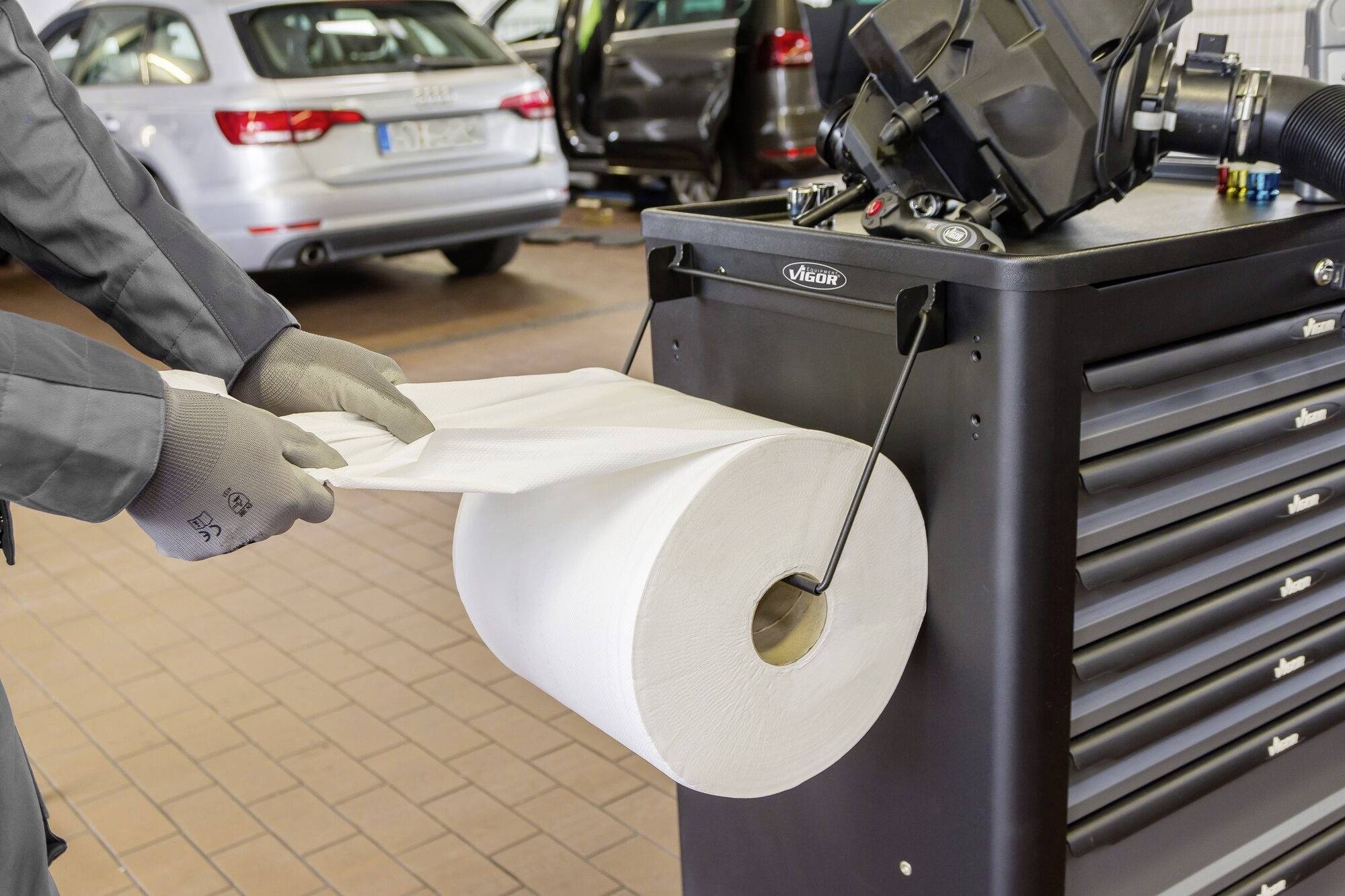 Une personne portant des gants tire un rouleau de papier à côté d'un établi dans un atelier mécanique. Des pneus de voiture sont visibles en arrière-plan.
