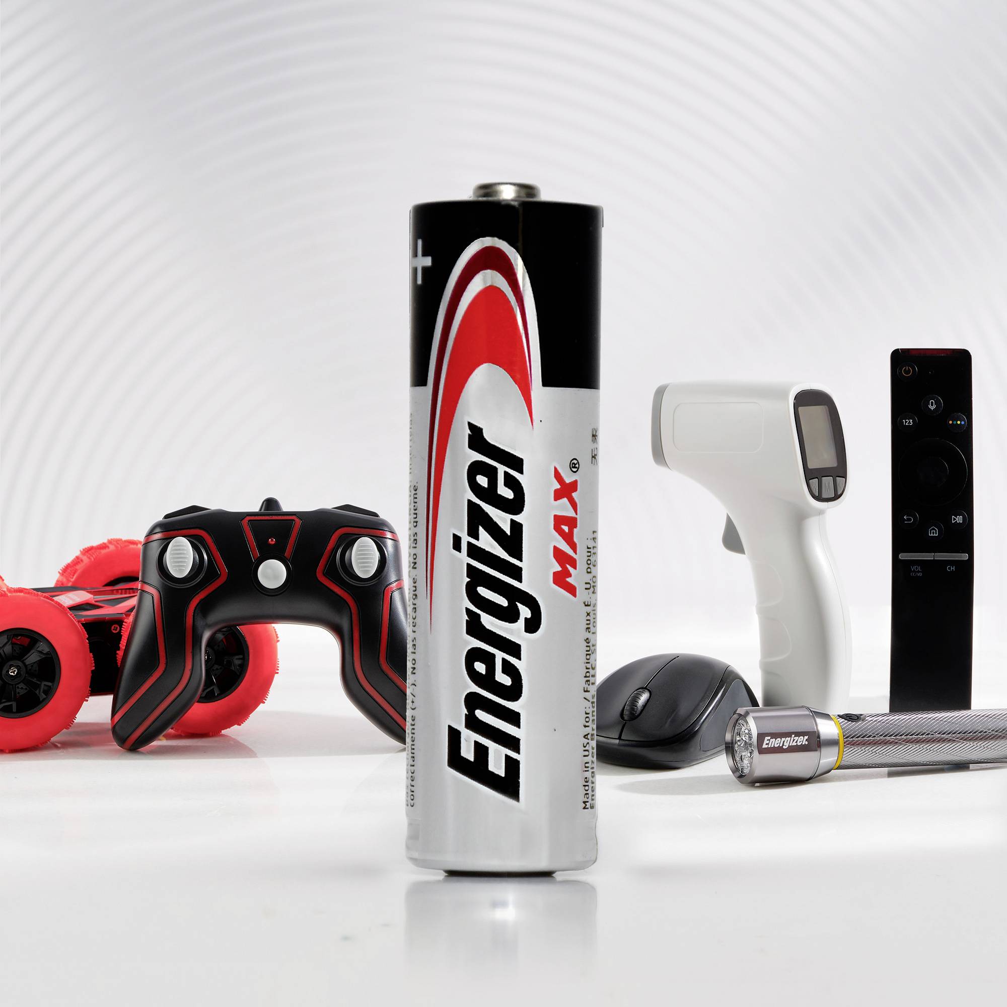 Batterie de marque 'Energizer Max' au premier plan, entourée de divers appareils électroniques tels qu'une télécommande et une manette de jeu.