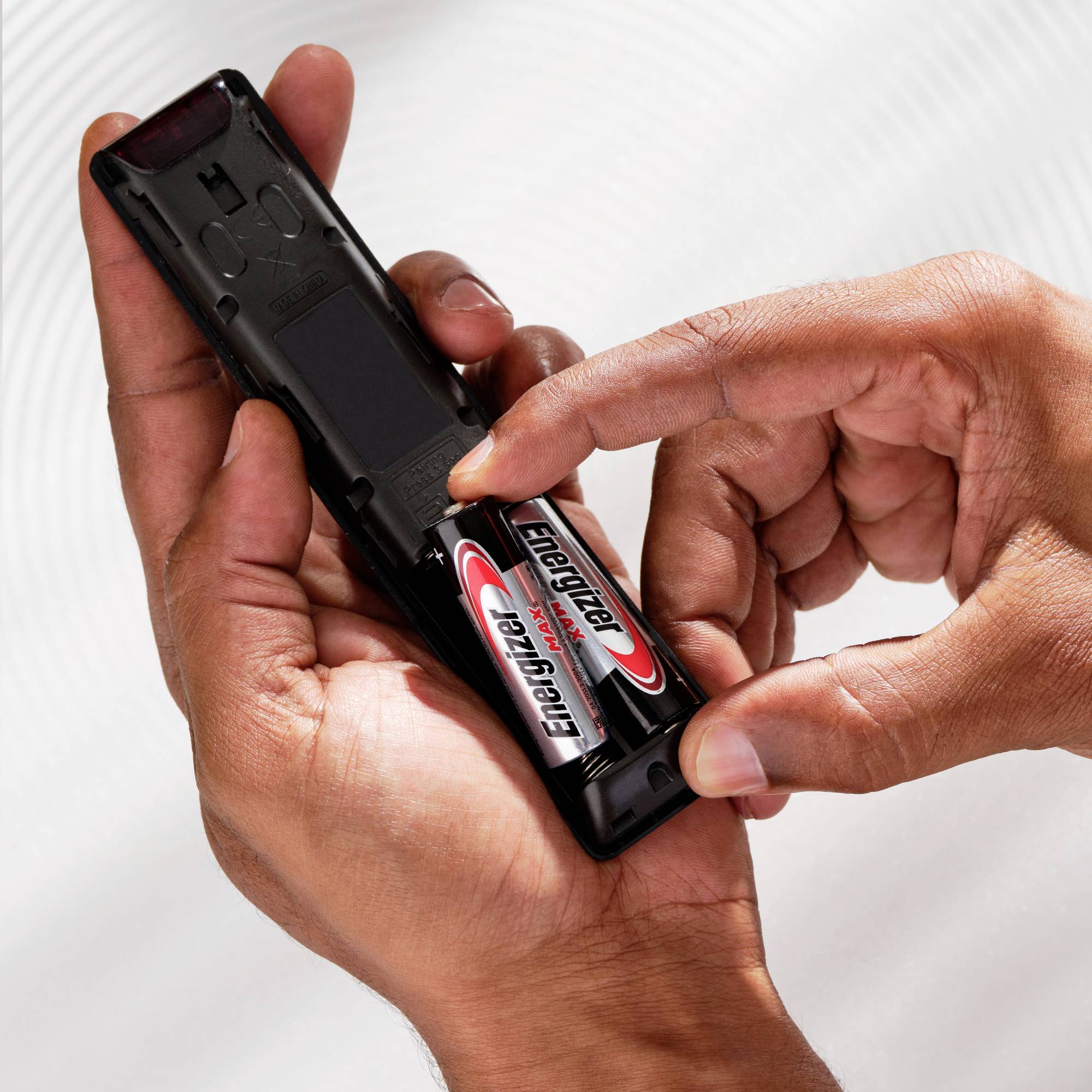 Une main insère des piles Energizer dans une télécommande.