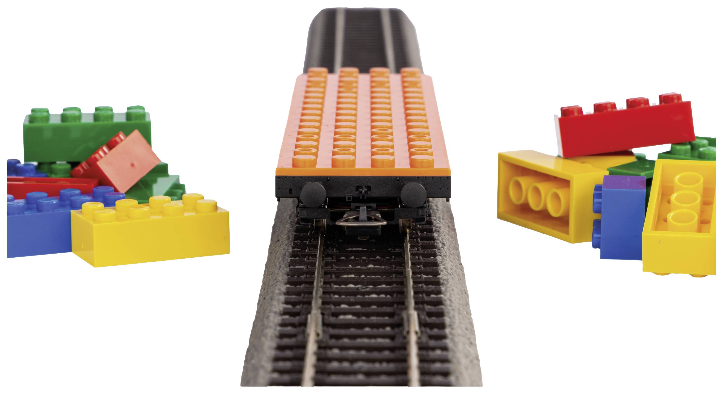 Un petit train de blocs roule sur des rails, entouré de briques LEGO colorées des deux côtés.