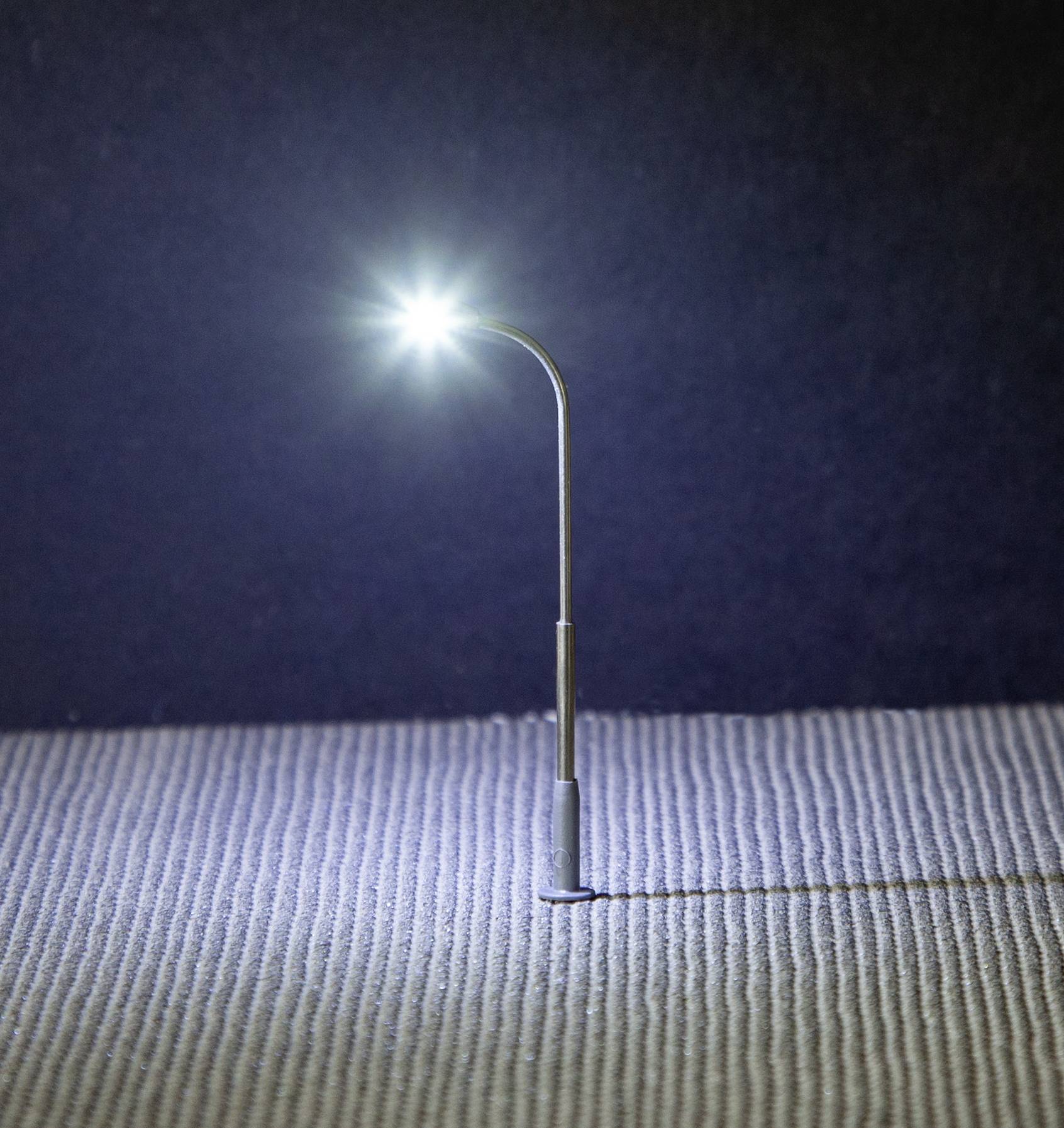 Une mini-lampadaire brille intensément sur un support texturé devant un arrière-plan sombre.