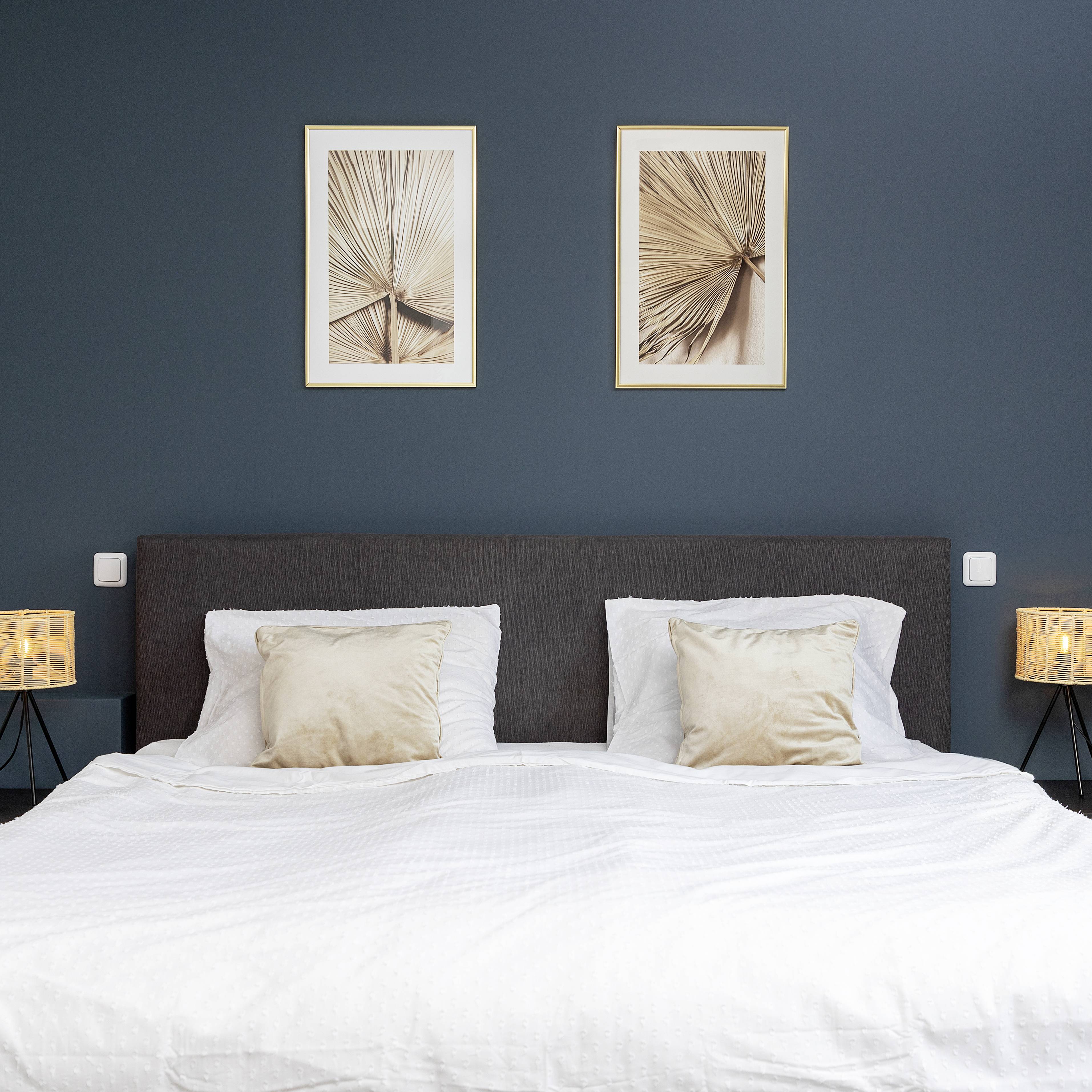 Une chambre moderne avec un lit double, deux coussins beiges, un mur bleu-gris et deux œuvres d'art abstraites au-dessus.