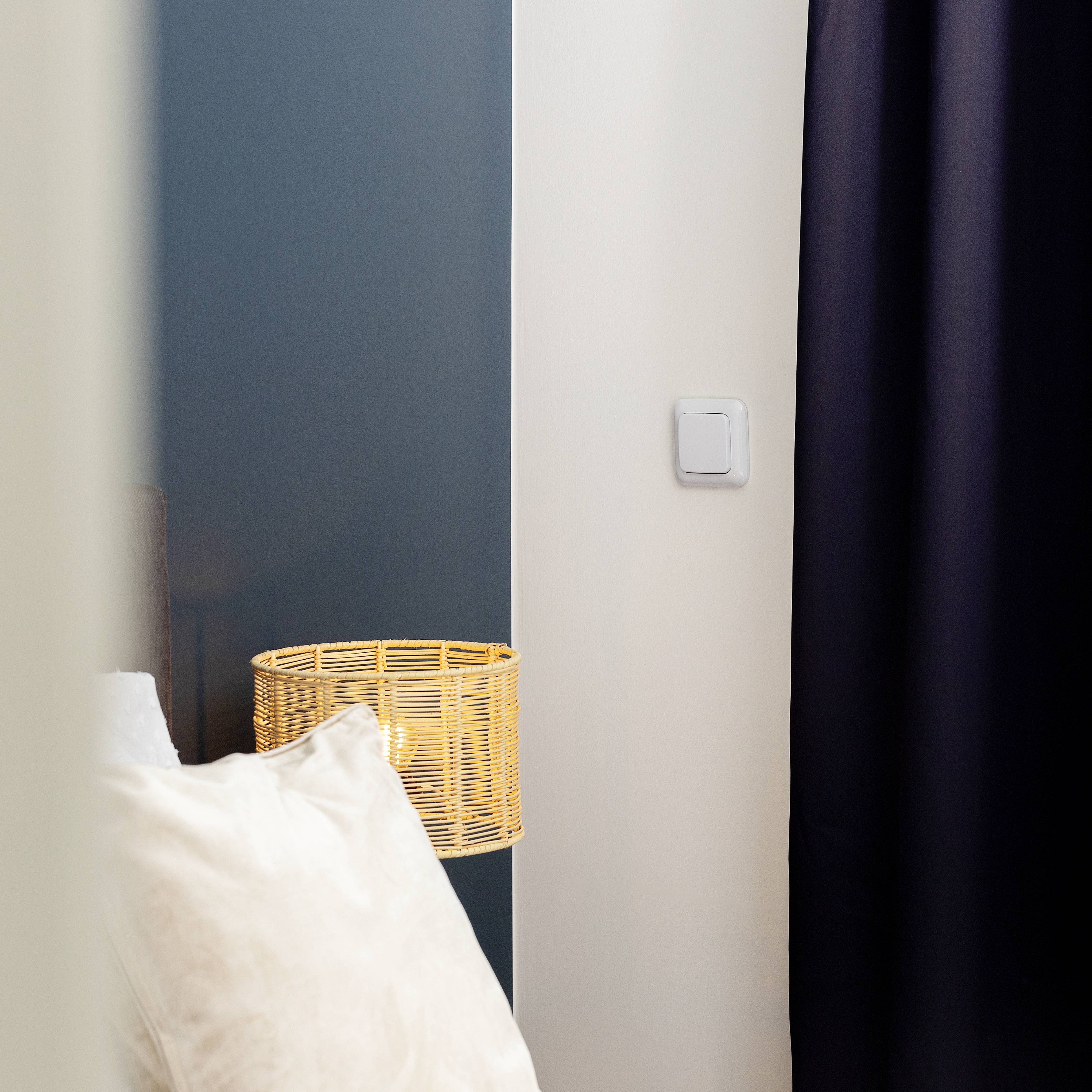 Une chambre confortable avec un coussin blanc au premier plan et un abat-jour rond et tressé sur une table.