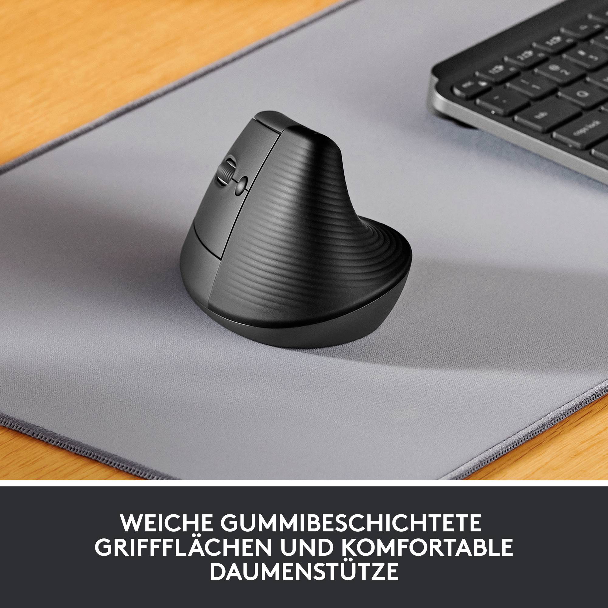 Une souris d'ordinateur noire, verticale, avec des surfaces de préhension revêtues de caoutchouc, est posée sur un bureau à côté d'un clavier.
