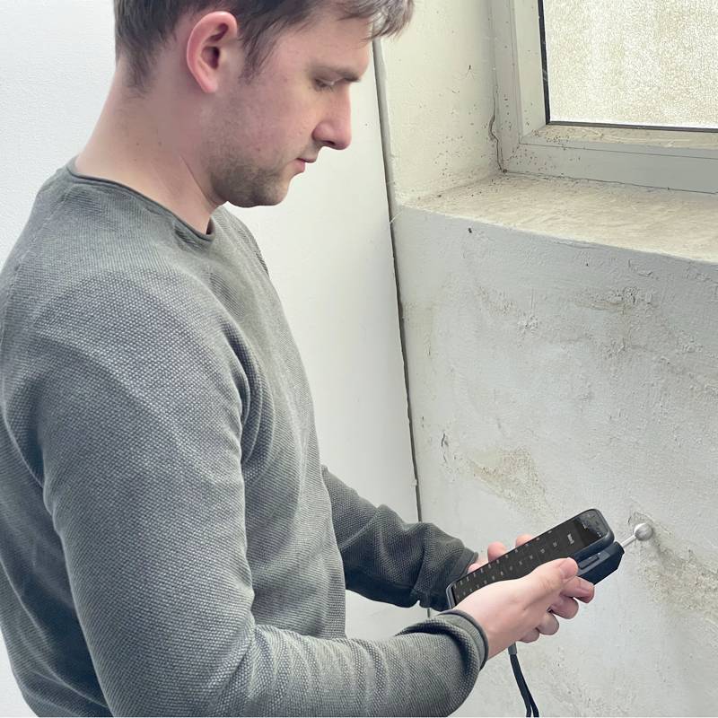 Un homme fore un trou dans un mur à côté d'une fenêtre et tient une perceuse.