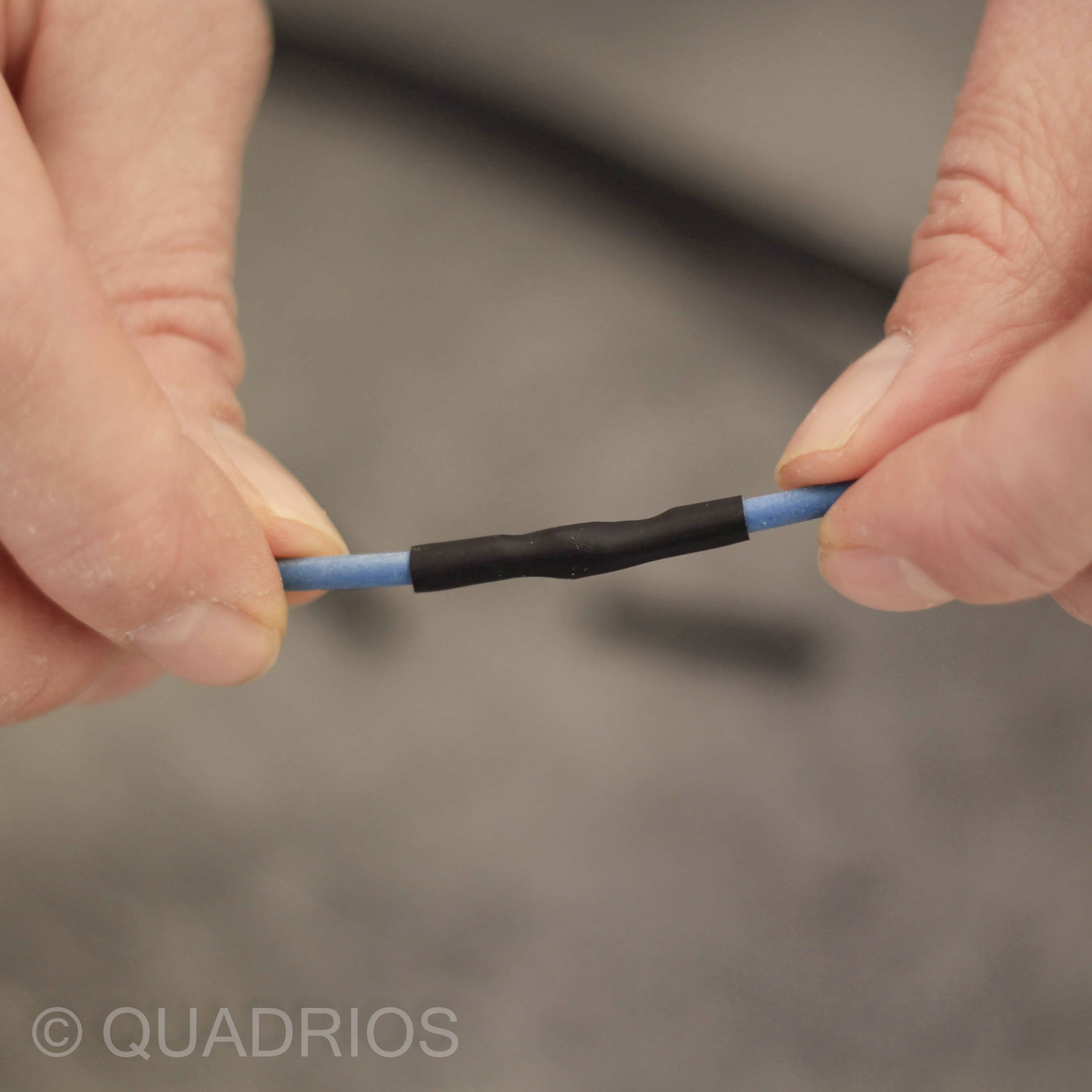 Deux mains tiennent un câble bleu avec une gaine thermorétractable noire au milieu.