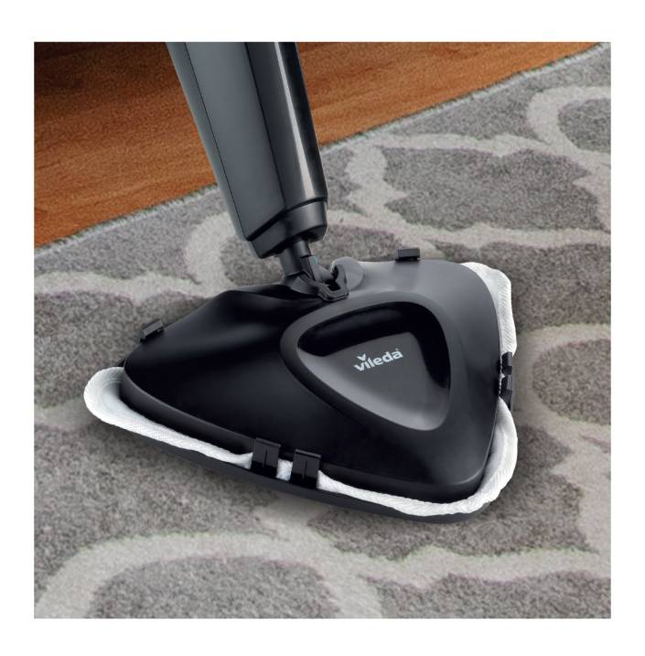 Un nettoyeur vapeur glisse sur un tapis. L'appareil est noir, triangulaire et portant le logo de 'Vileda'. Il nettoie efficacement le tapis.