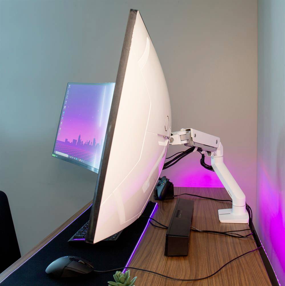 Un écran d'ordinateur moderne sur un bras ajustable, éclairé par des lumières roses et bleues, posé sur un bureau en bois.