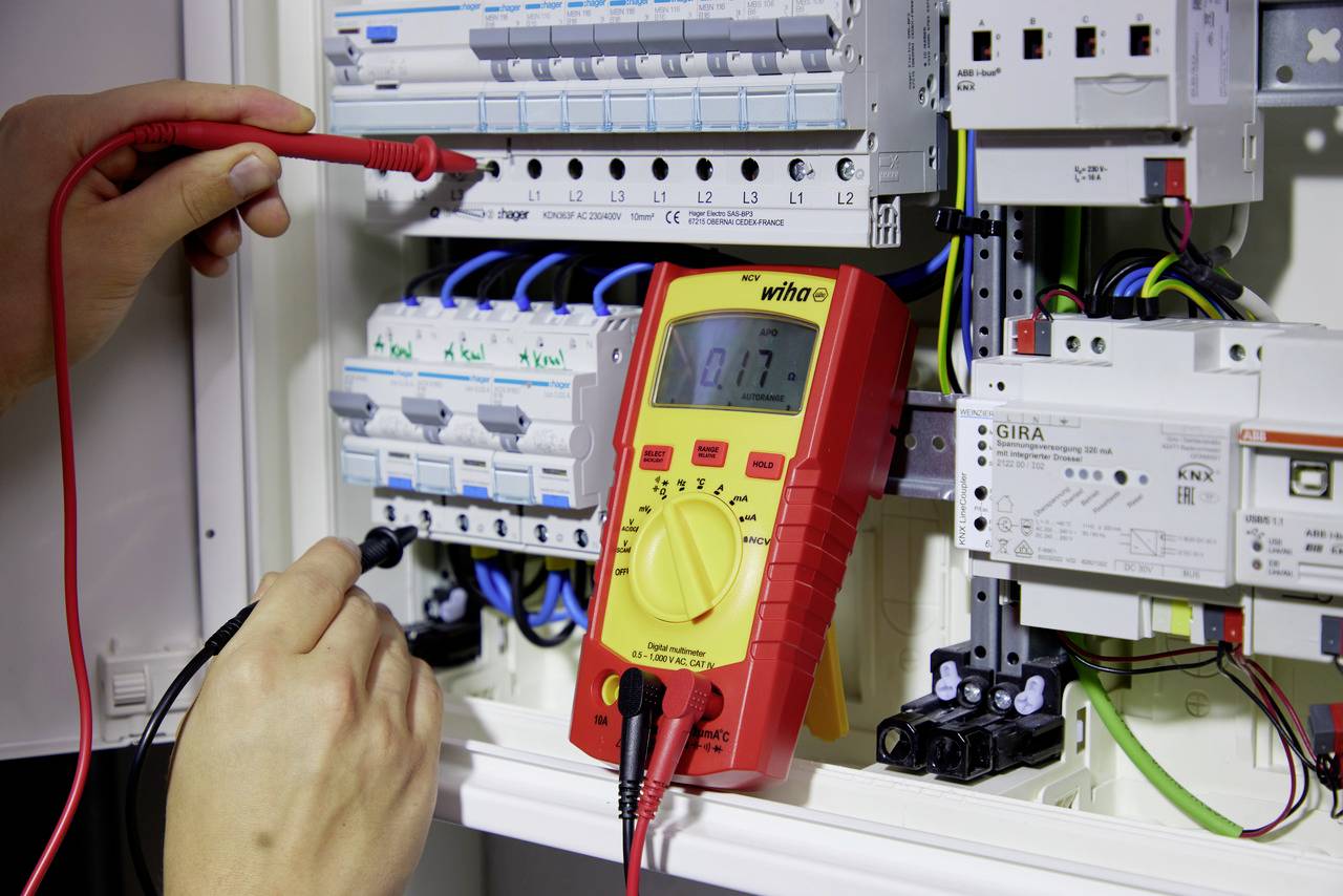 Une personne mesure la tension dans un tableau électrique à l'aide d'un multimètre afin de vérifier les valeurs électriques.
