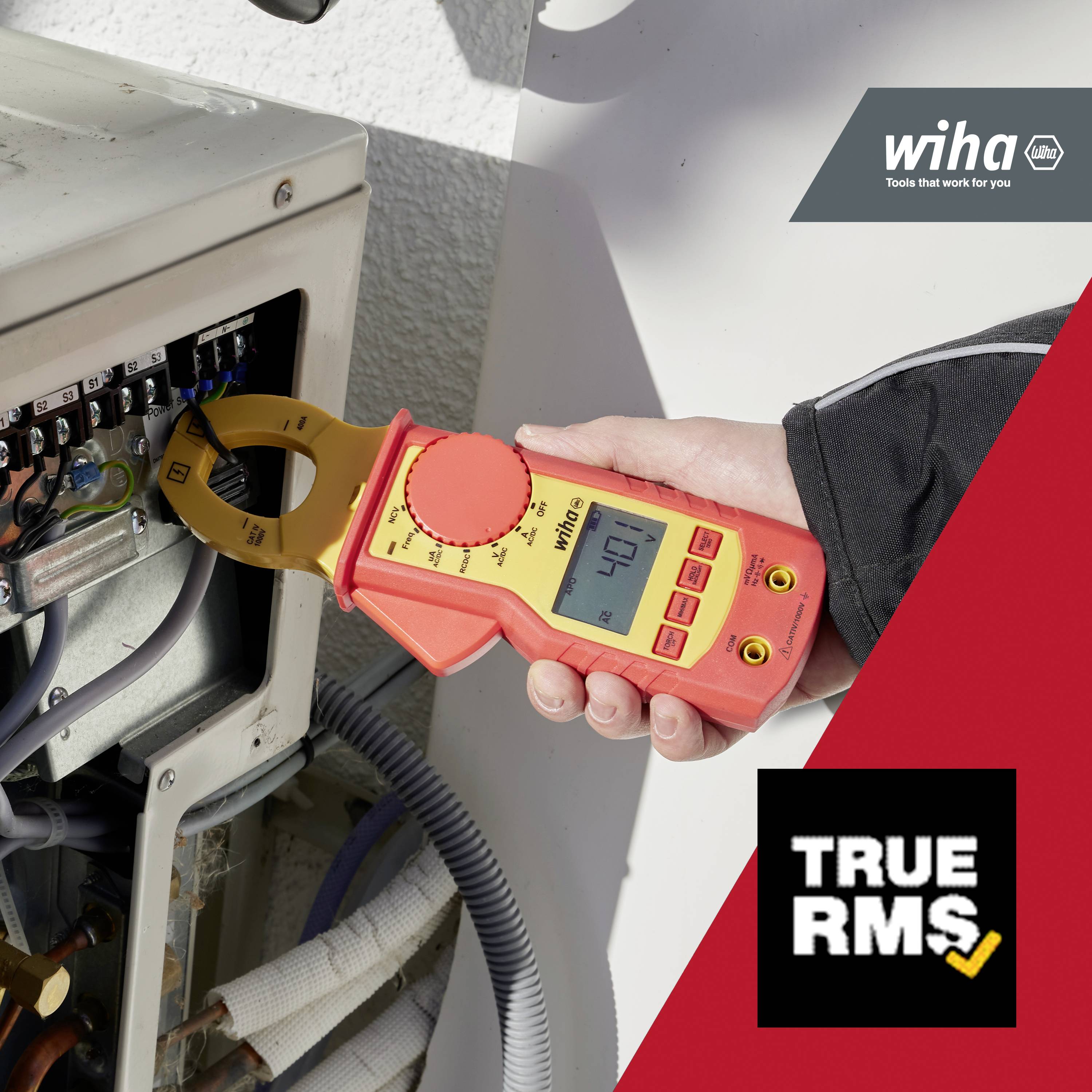 Une personne mesure le courant avec une pince ampèremétrique rouge et jaune sur un boîtier électrique. Le logo 'Wiha' est visible en arrière-plan.