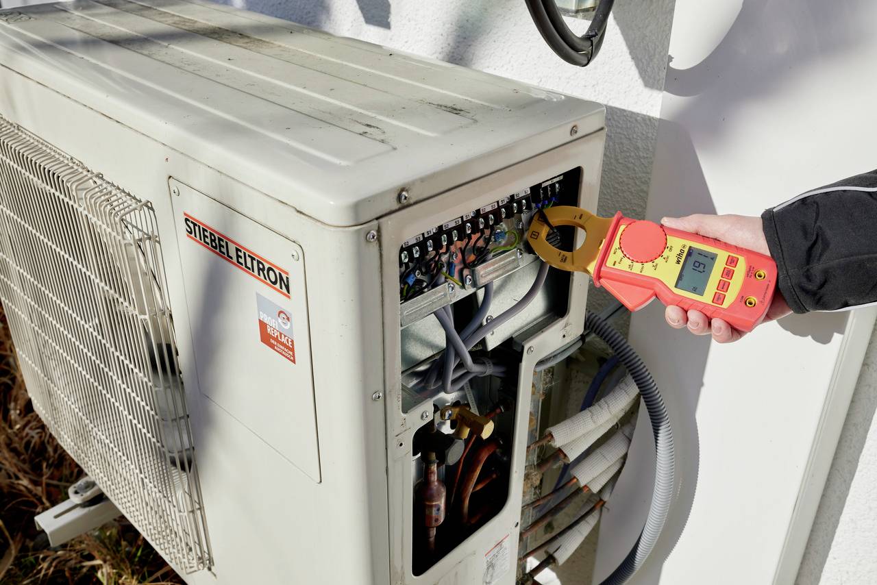 Une personne mesure le flux électrique sur une unité de climatisation à l'aide d'un appareil de mesure numérique afin de vérifier son bon fonctionnement.