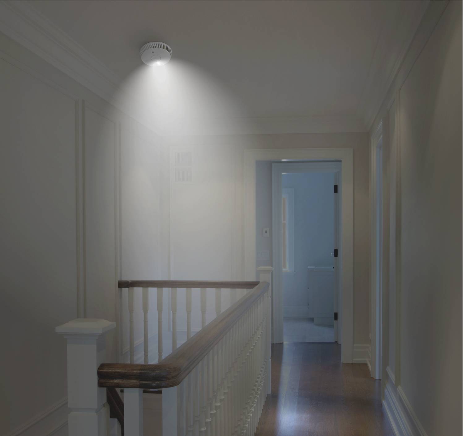 Un couloir éclairé avec un détecteur de fumée au plafond. Derrière le couloir, une porte ouverte mène à une salle de bain.