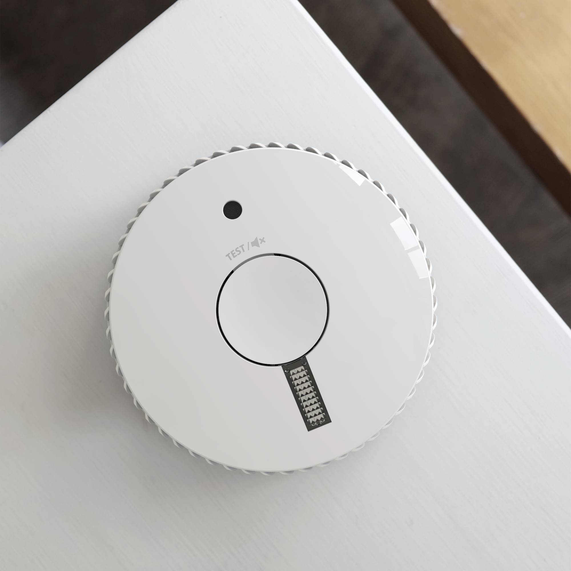 Un détecteur de fumée rond sur un plafond blanc. Il a un grand bouton au centre portant l'inscription 'TEST'.