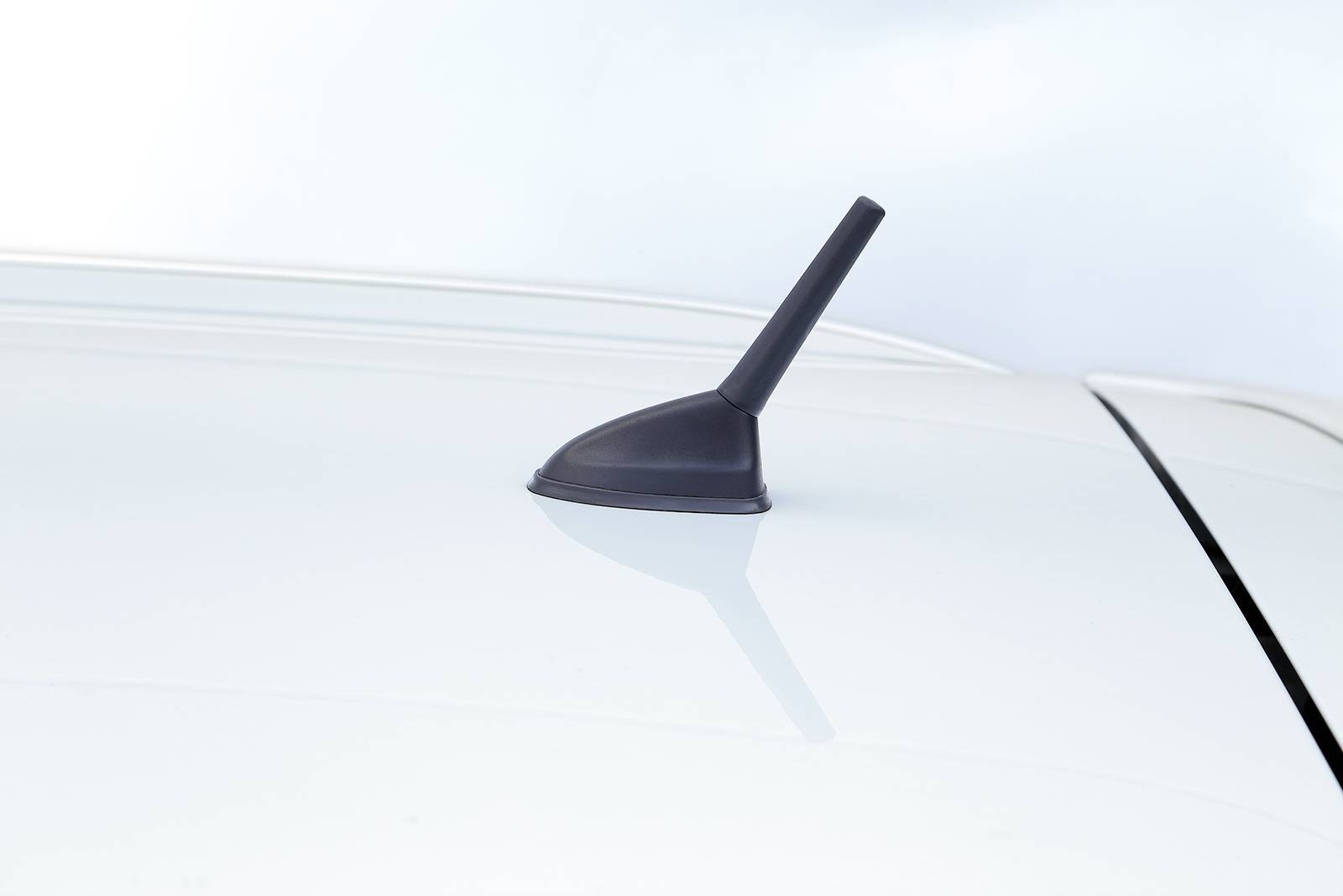 Antenne automatique sur un toit de voiture blanc devant un ciel nuageux.