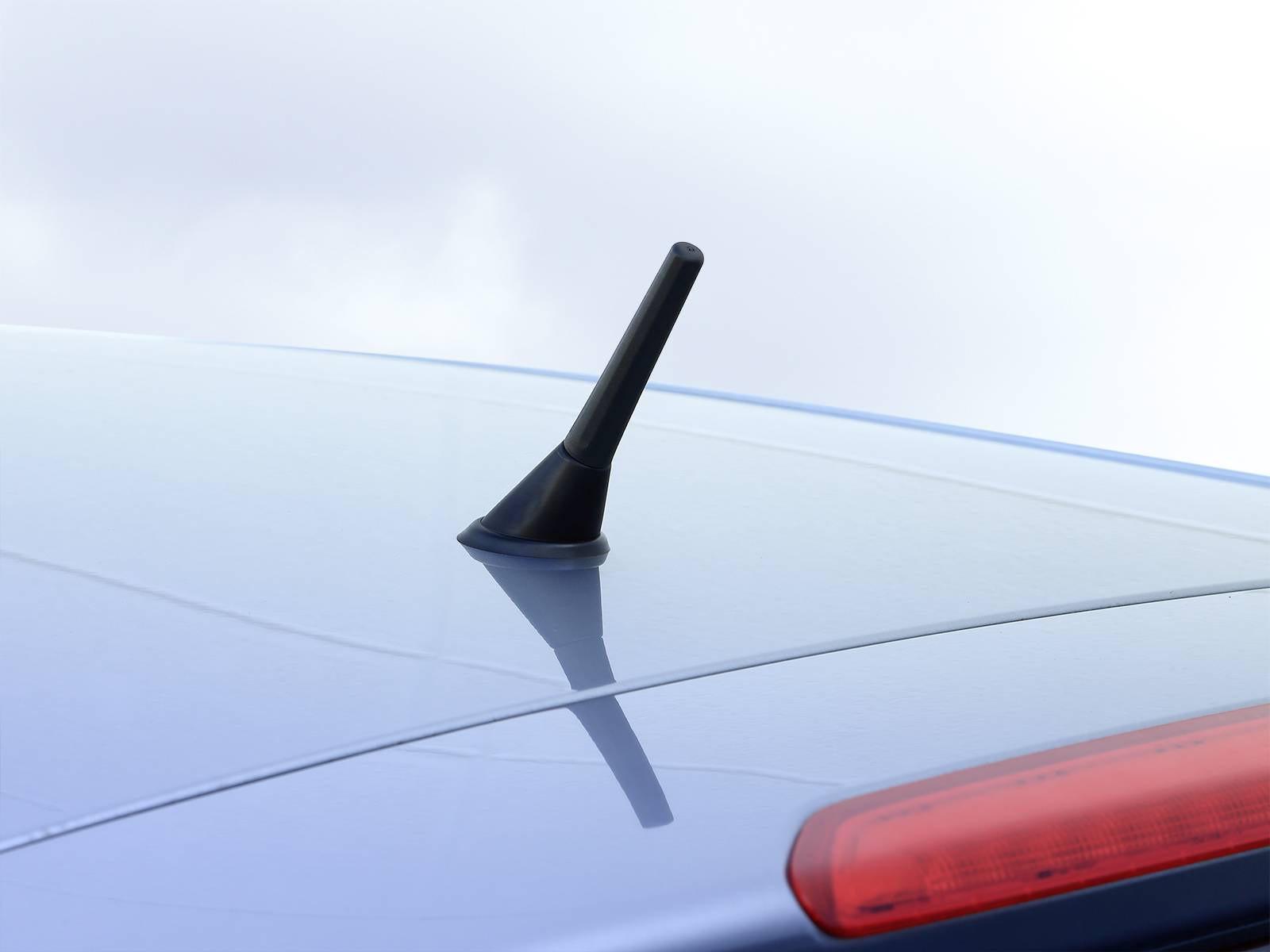 Une courte antenne noire sur le toit d'une voiture argentée, photographiée sous un ciel nuageux.