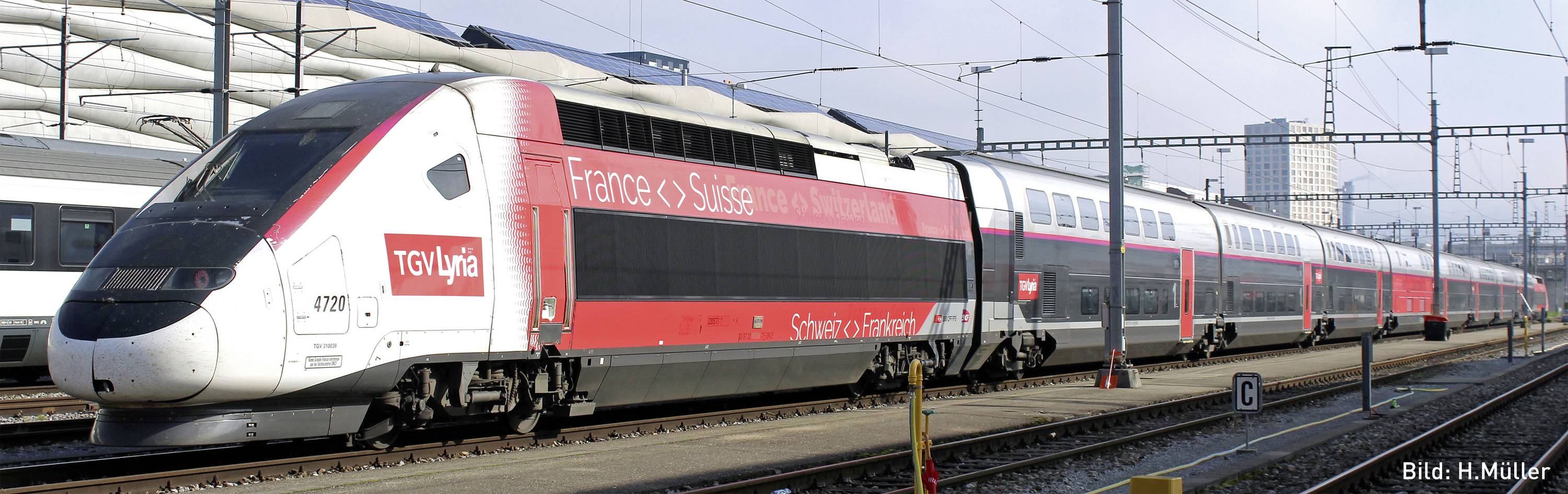 Un train à grande vitesse rouge et blanc portant l'inscription 'France-Suisse' est stationné sur un quai dans une ville.
