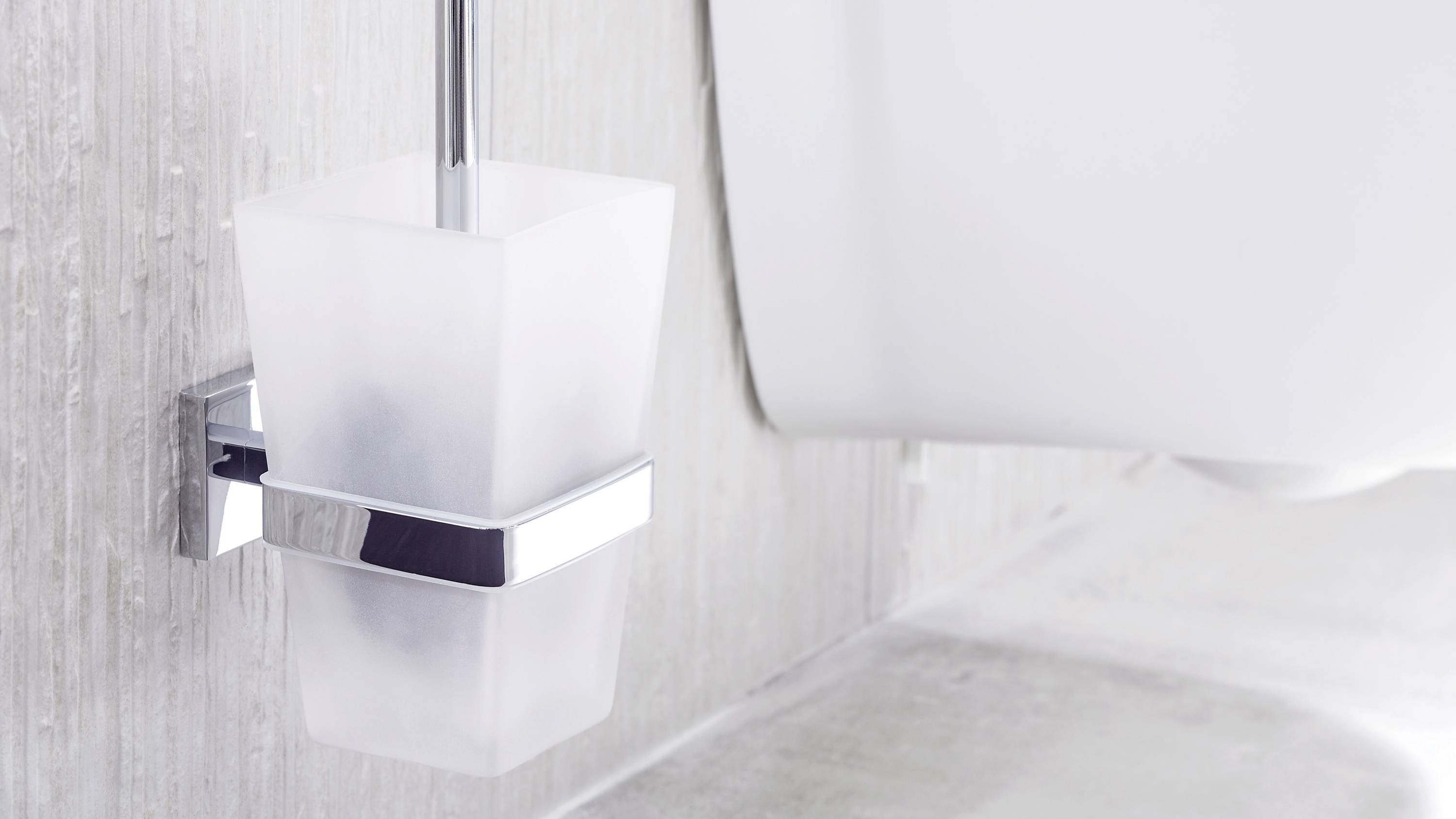 Un gobelet à brosse à dents en verre satiné dans une salle de bain moderne, monté au mur, à côté d'un lavabo blanc.