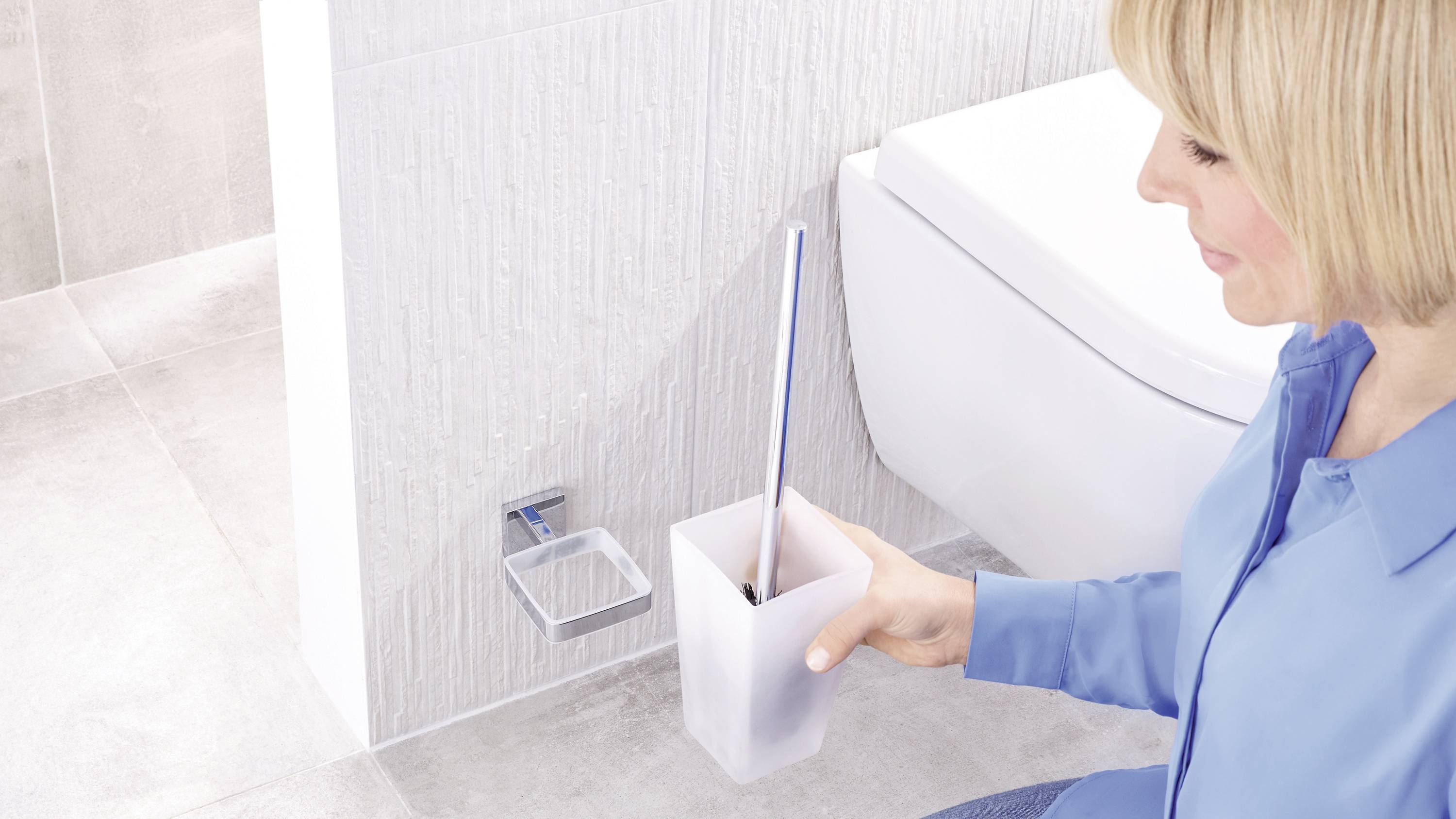 Une personne nettoie la salle de bain avec une brosse de toilettes. Les toilettes blanches sont visibles en arrière-plan.